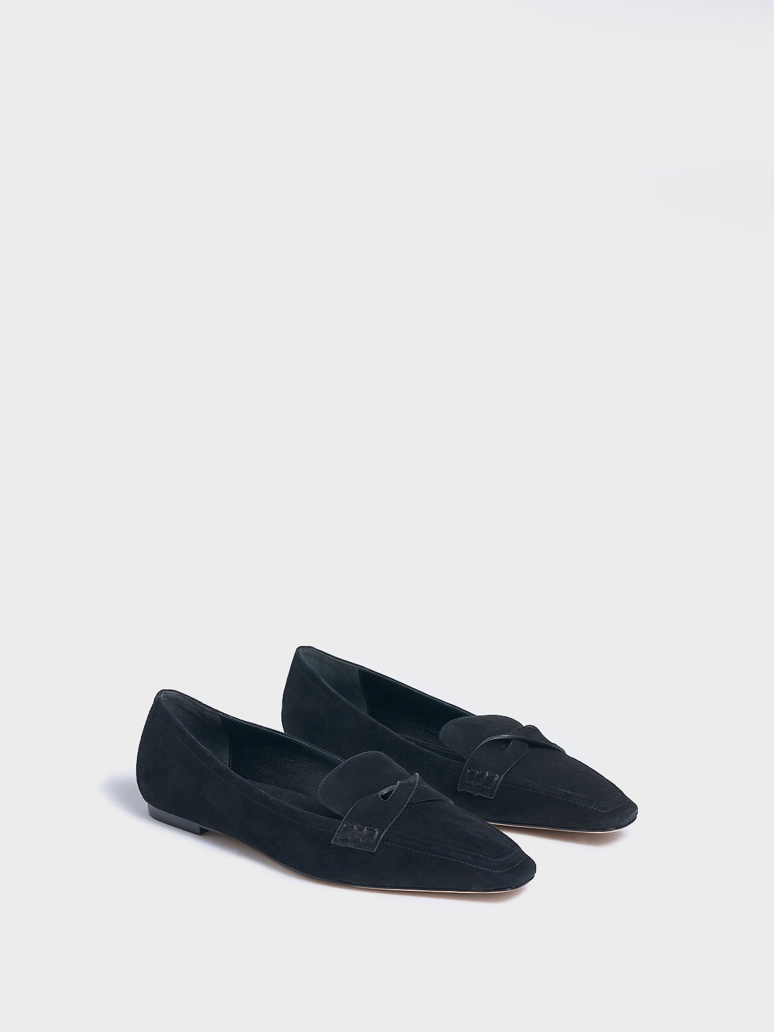 Angle view of a pair of black suede penny loafers with a twist detail.