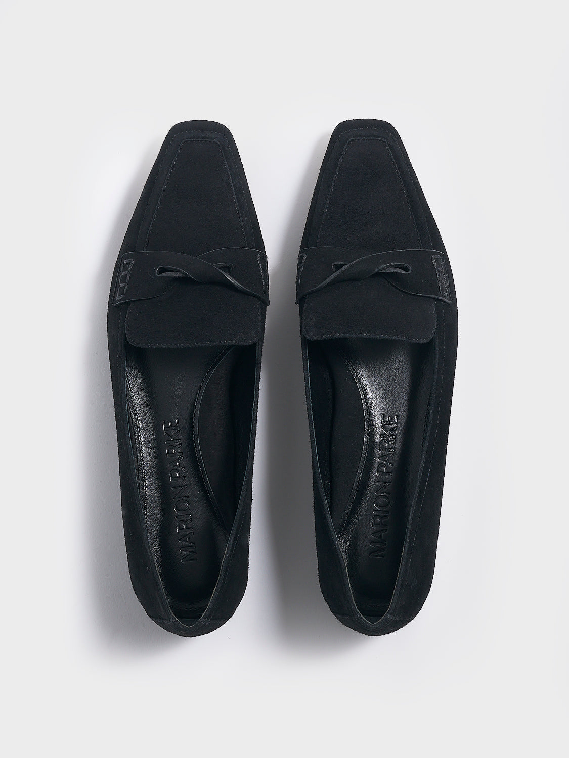 Top view of a pair of black suede penny loafers with a twist detail.
