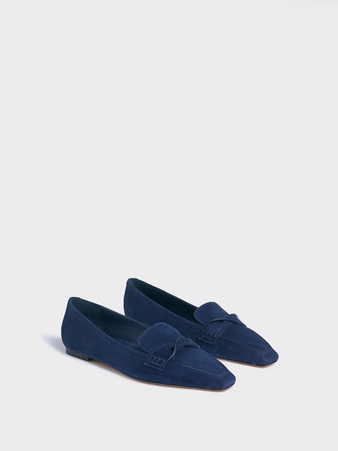 Angle view of a pair of navy blue suede penny loafers with a twist detail.