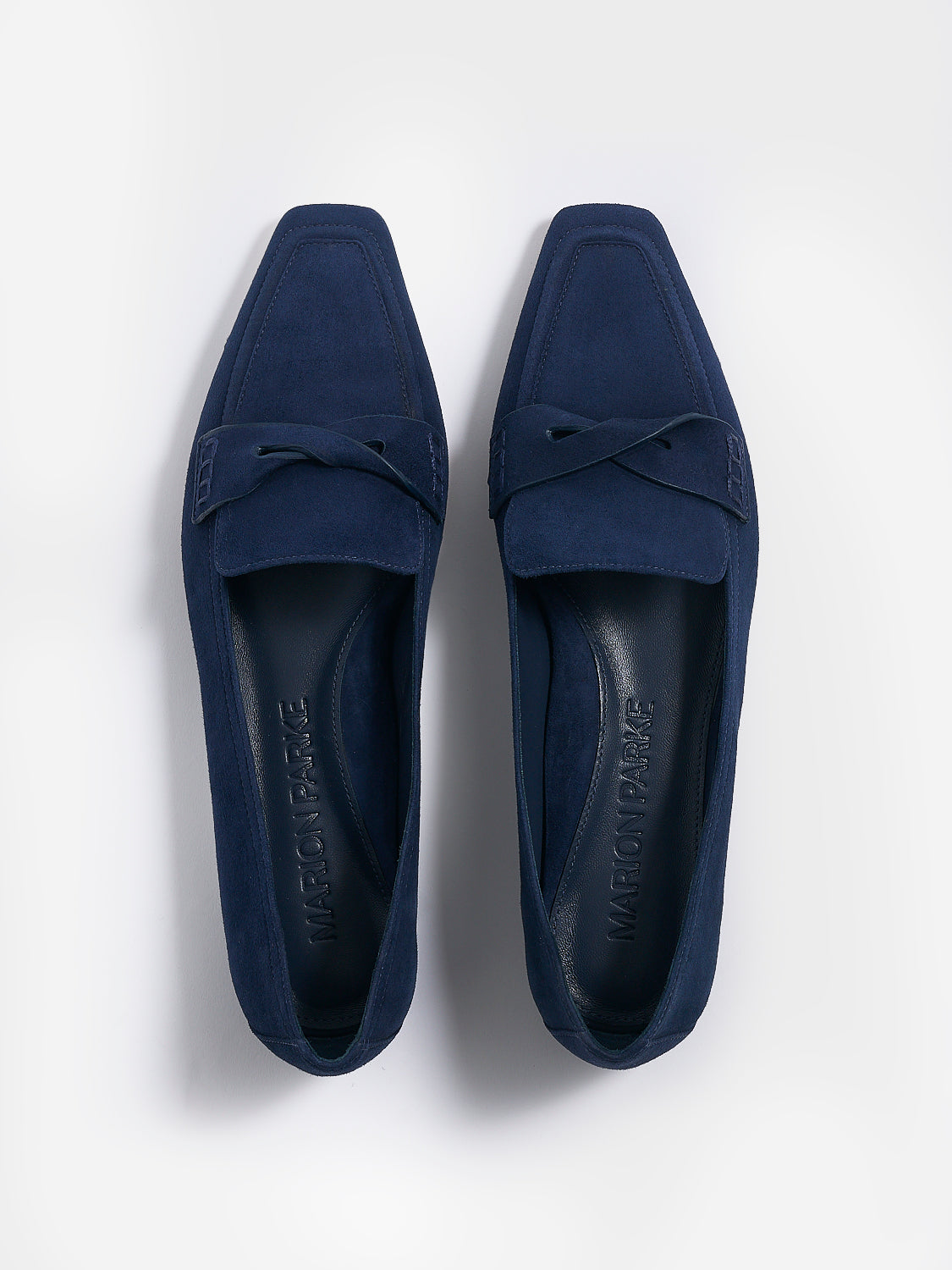 Top view of a pair of navy blue suede penny loafers with a twist detail.
