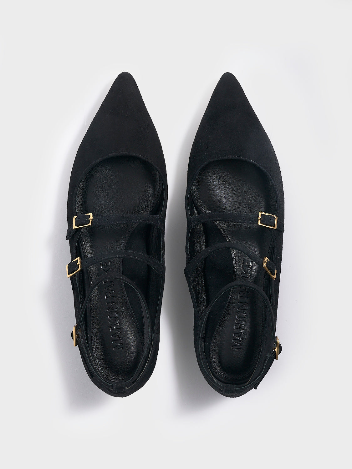 Angle view of a pair of black suede mary jane flats with adjustable straps and a pointed toe.
