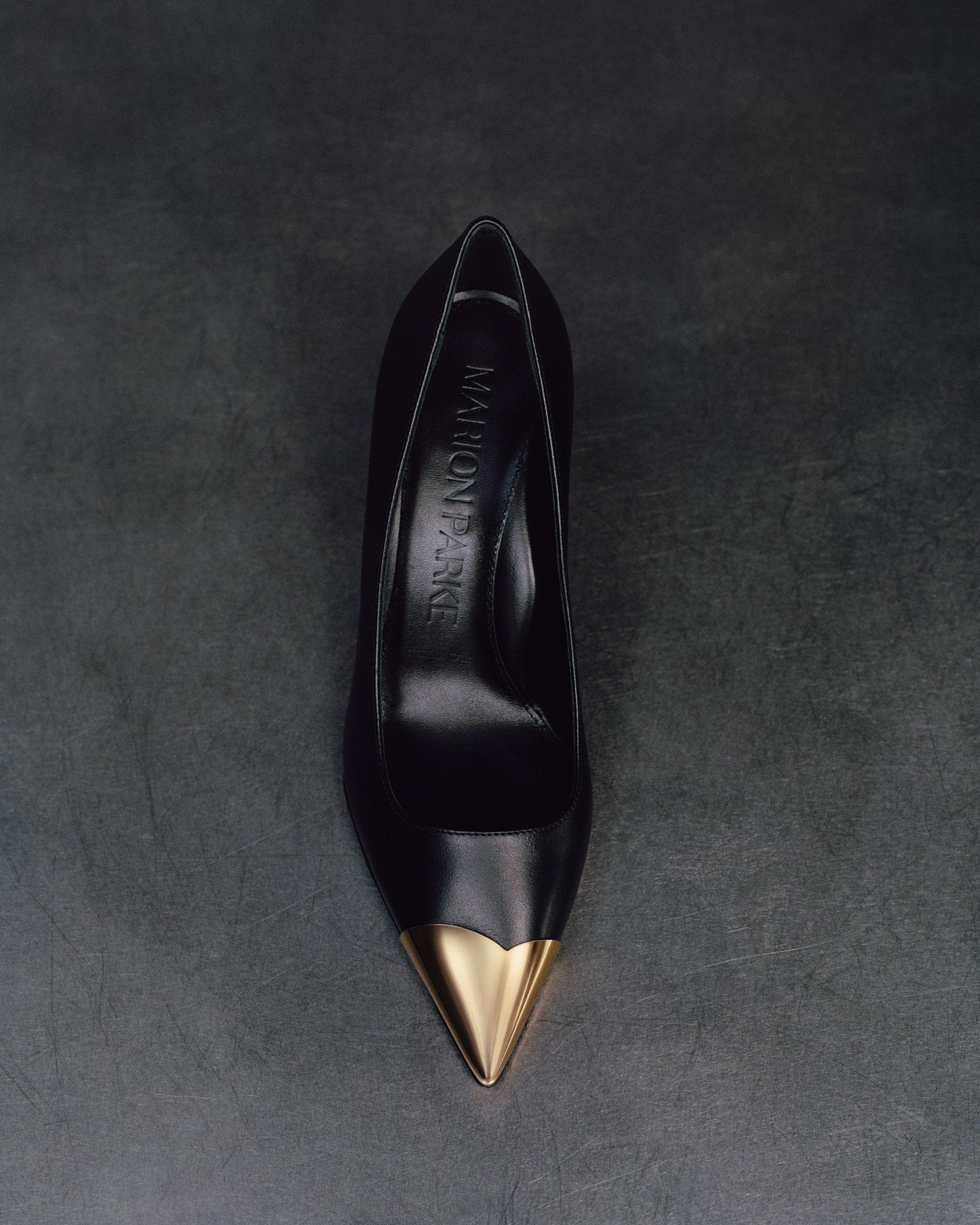 Top view of a black leather stiletto heel pump with a gold metallic toe cap and a pointed toe.