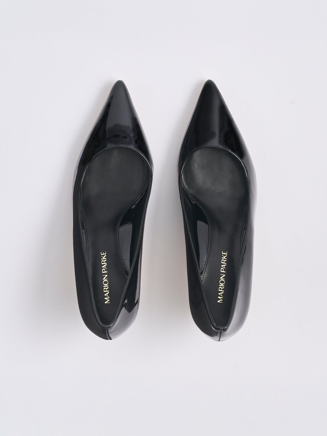 Top view of a pair of black patent leather stiletto heel pumps with a pointed toe.