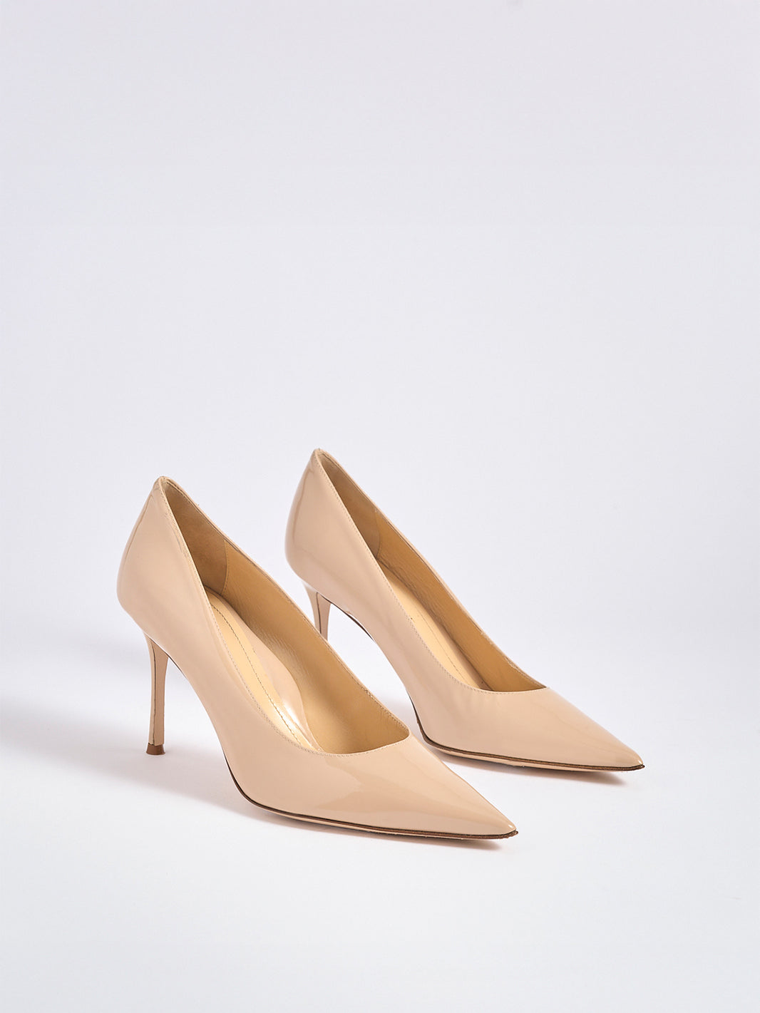 Angle view of a pair of powder patent leather high stiletto heel pumps with a pointed toe.