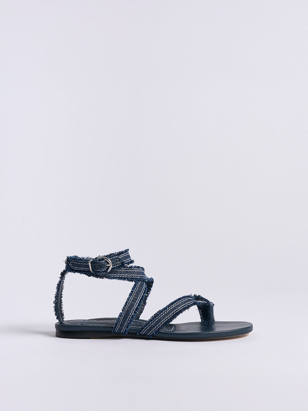 Profile view of a navy blue denim thong flat sandal with a rounded toe