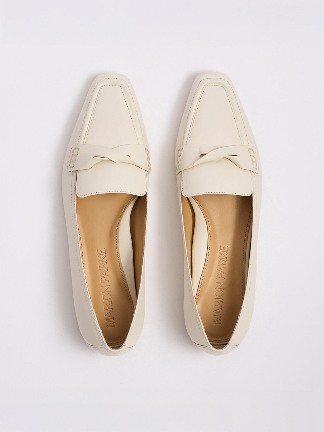 Top view of a pair of light cream leather penny loafers with a twist detail.