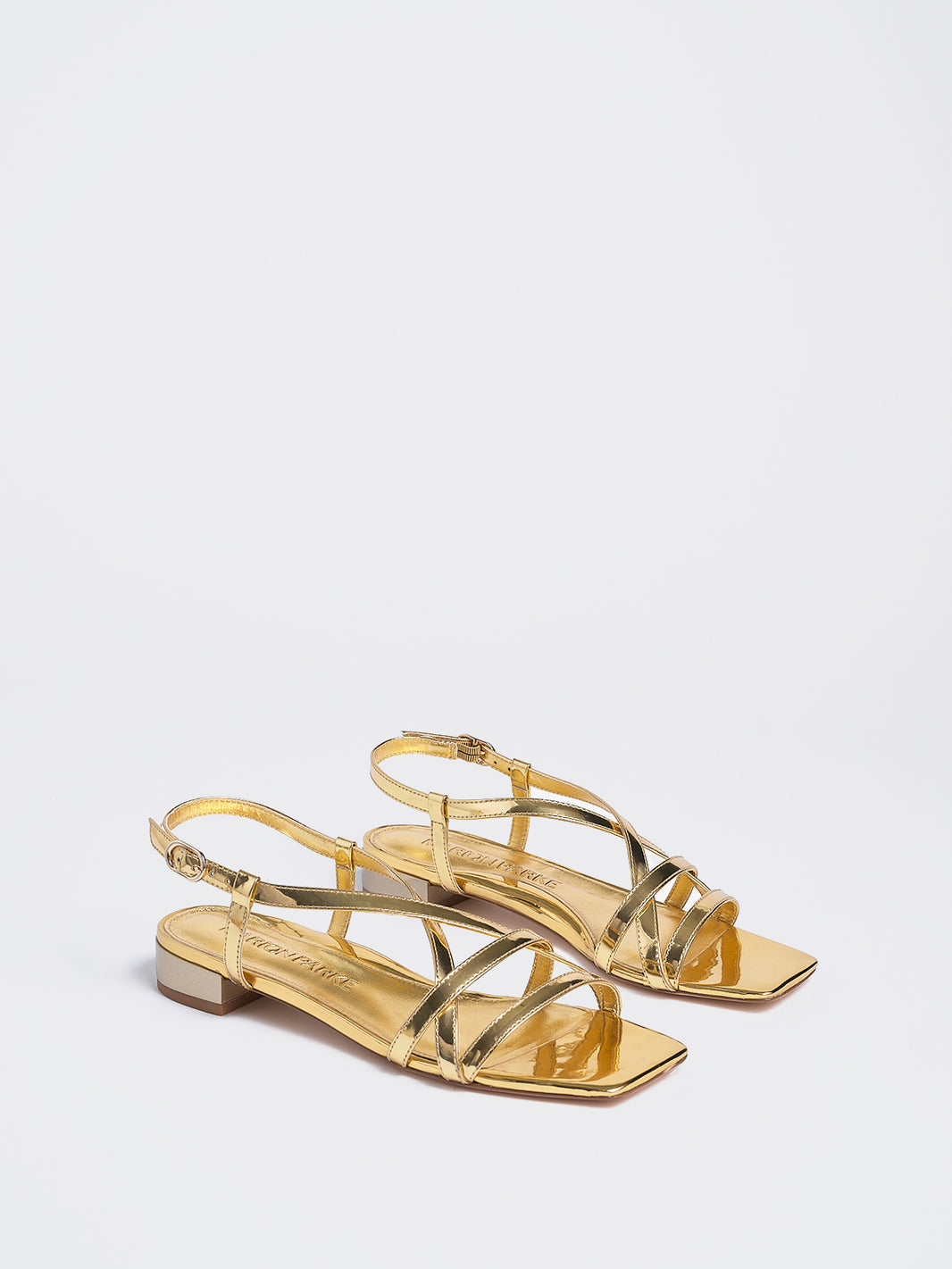 Angle view of a pair of gold metallic leather flat strappy sandals.