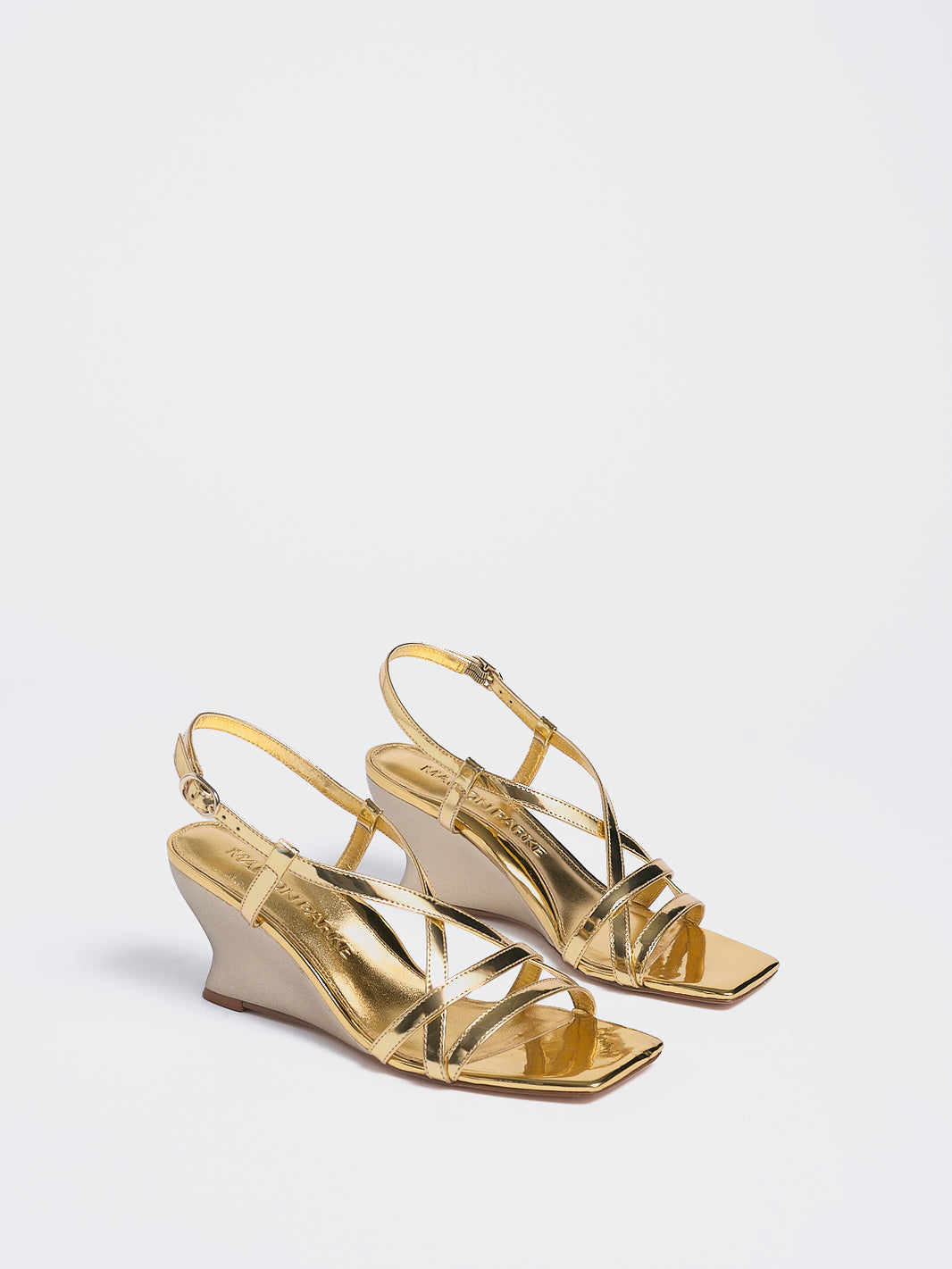 Angle view of a pair of gold metallic leather strappy sandals with a sculptural wedge.