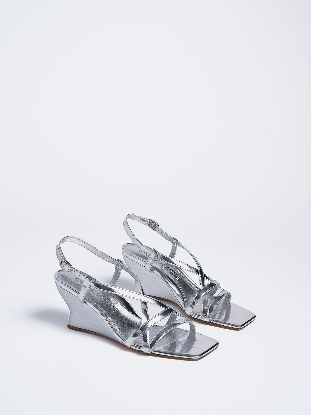 Angle view of a pair of silver metallic leather strappy sandals with a sculptural wedge.