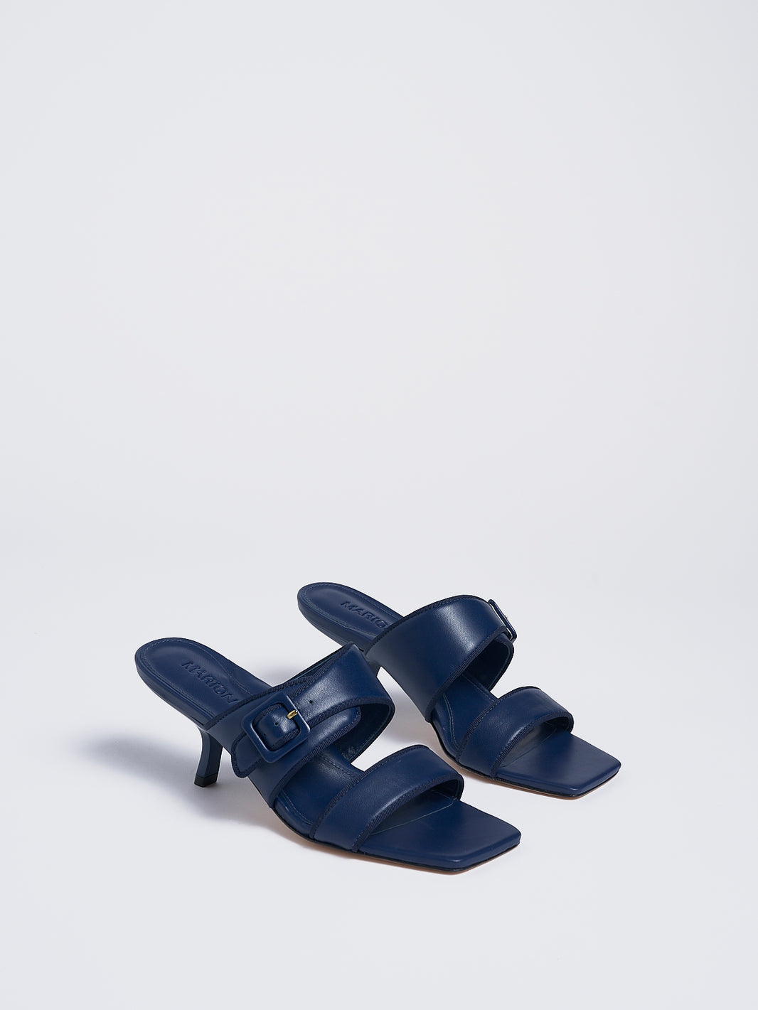 Angle view of a pair of navy leather slide kitten heel sandals with a buckle detail.