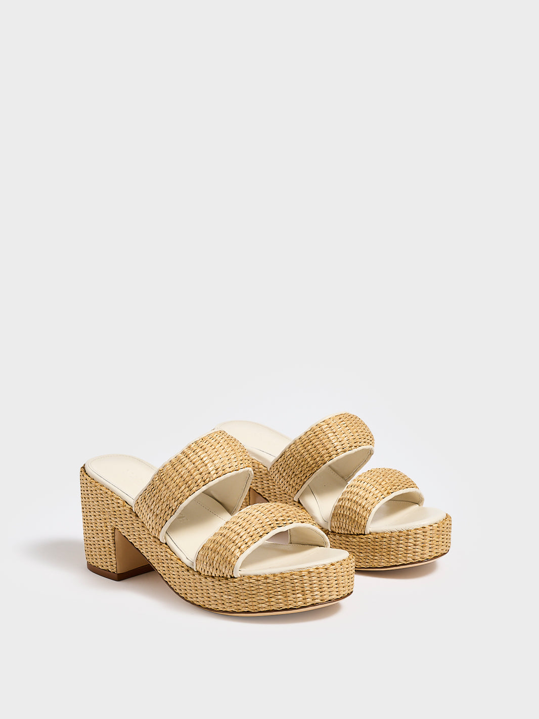 Angle view of a pair of raffia platform sandals with a light cream leather trim and puffed straps.