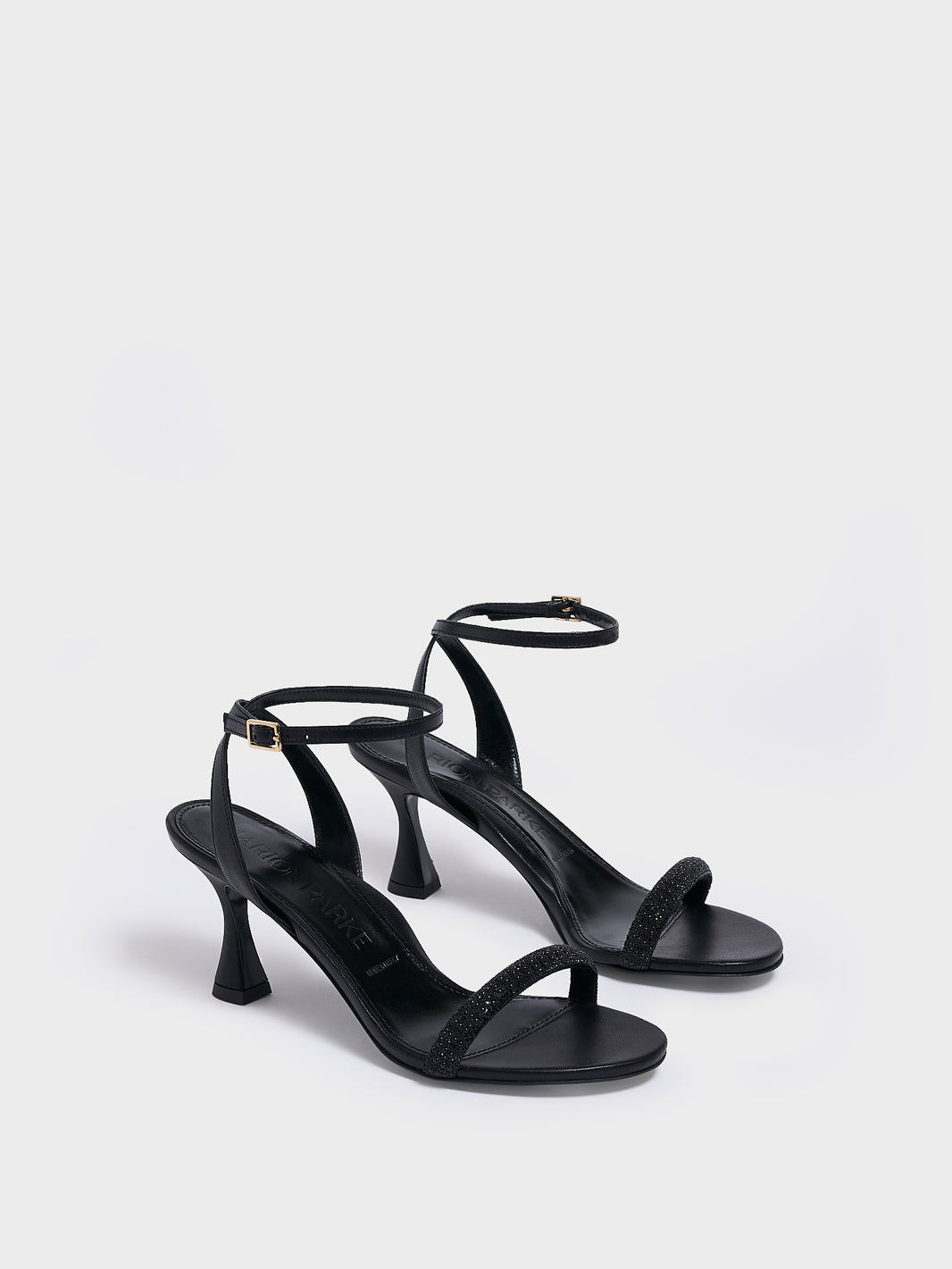 Angle view of a pair of black leather high heel sandals with a crystal embellished toe strap and adjustable ankle strap.