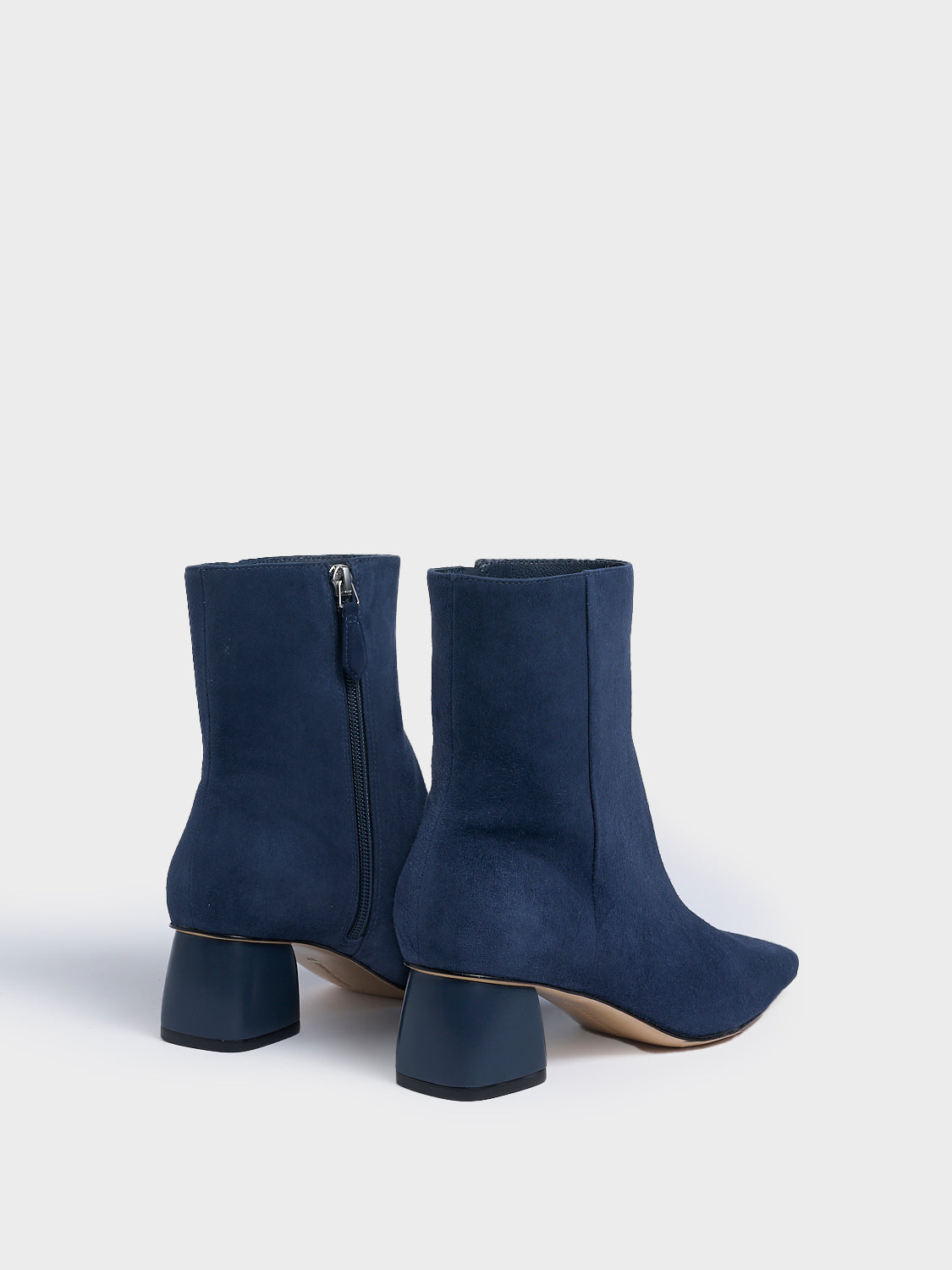 Back view of a pair of navy suede ankle booties with a rounded heel shape, zipper closure, and square toe.