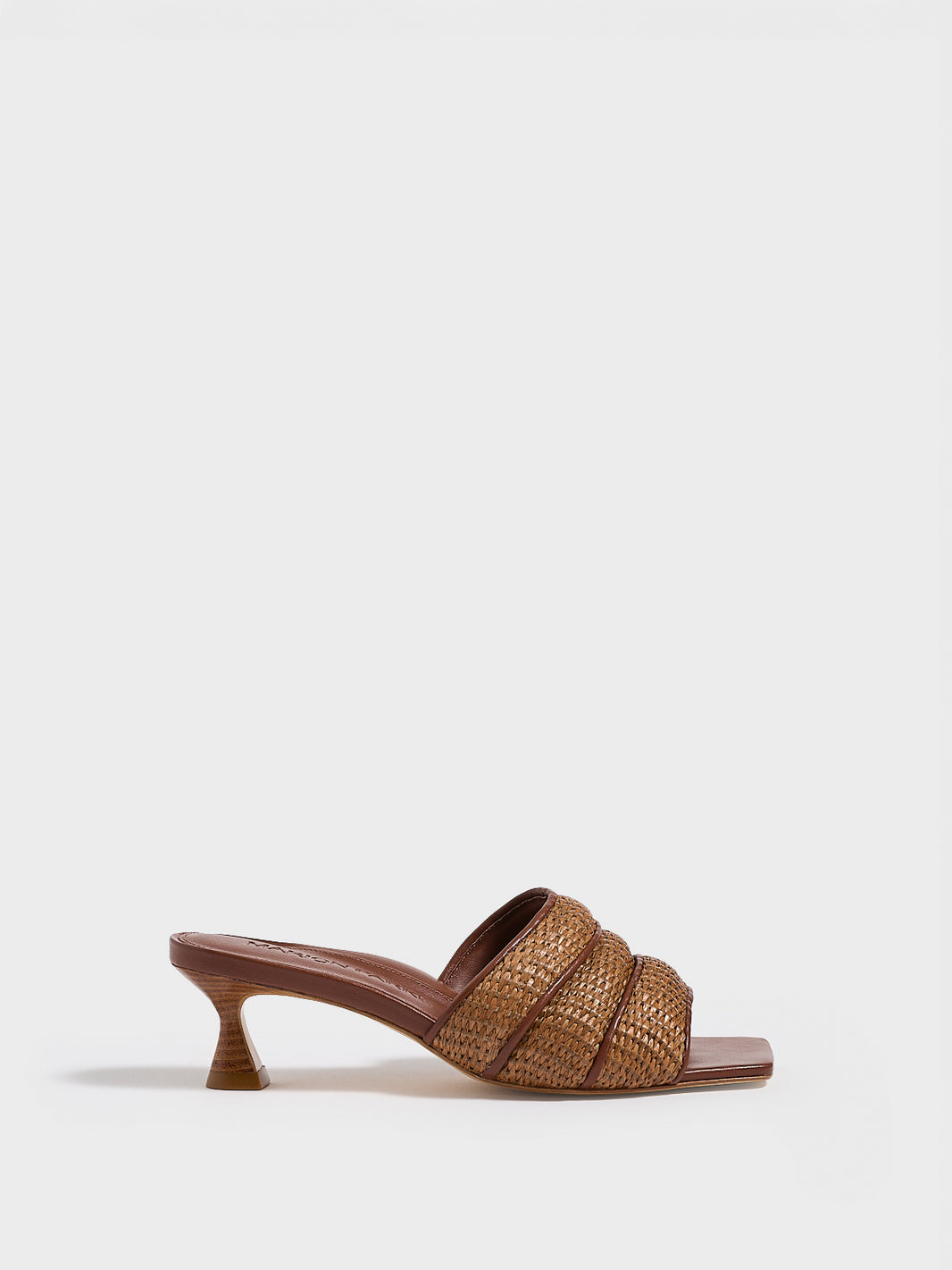 Profile view of a dark brown raffia slide kitten heel with a leather trimmed puffy strap detail.