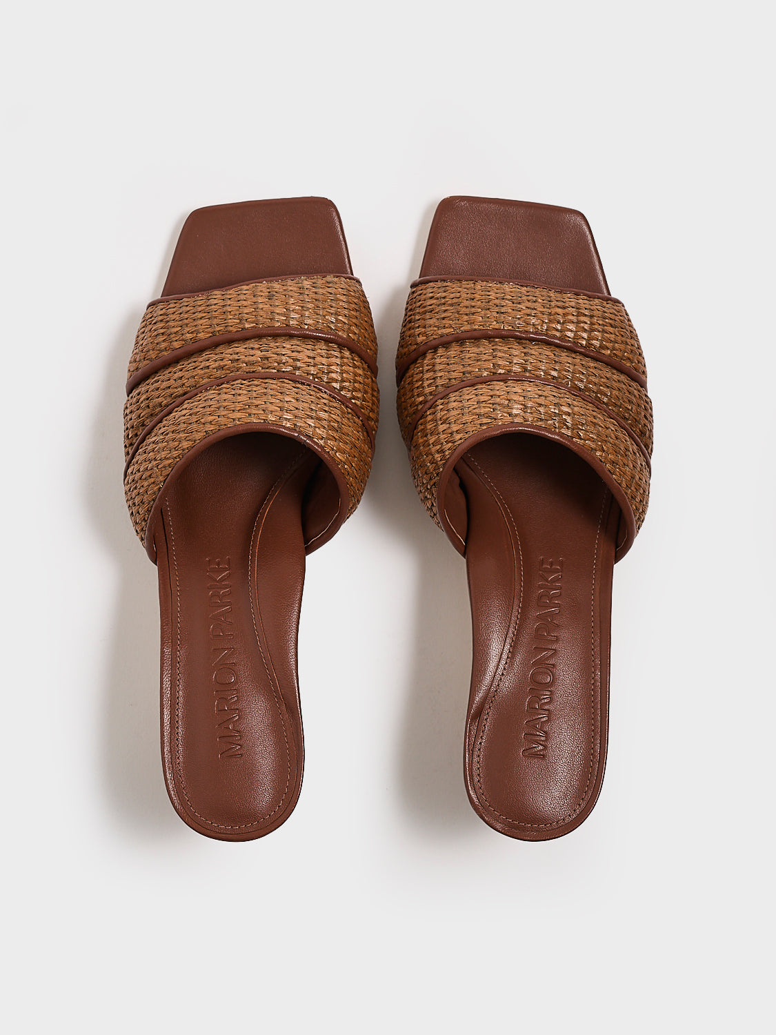 Top view of a pair of dark brown raffia slide kitten heels with a leather trimmed puffy strap detail.