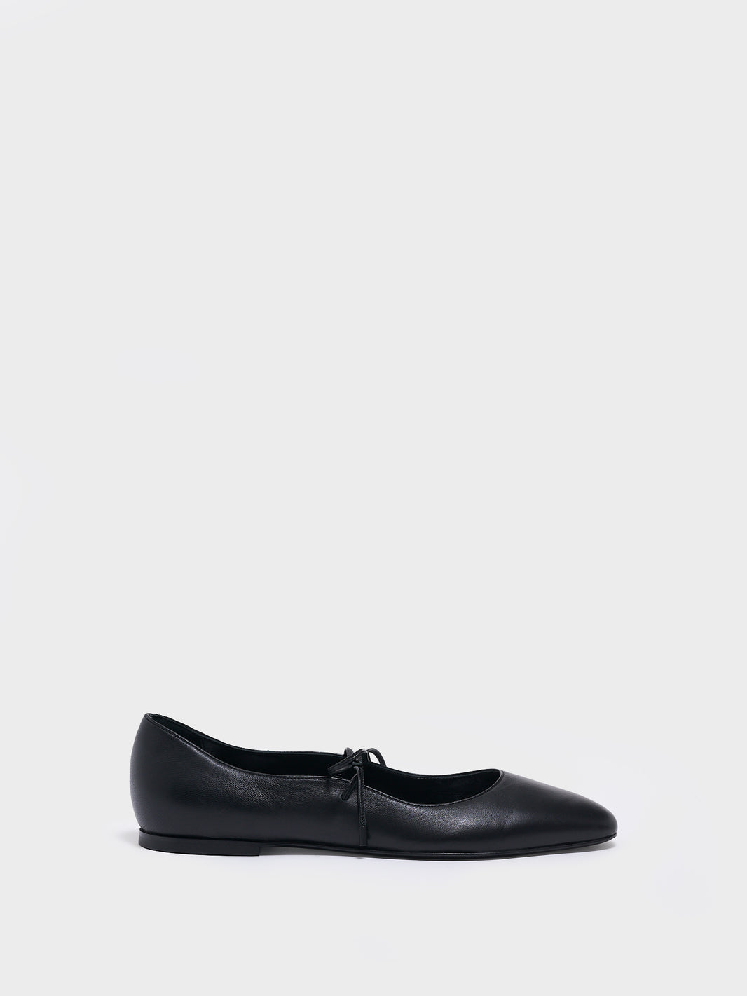 Profile view of a black leather ballet flat with an almond toe and tie detail.