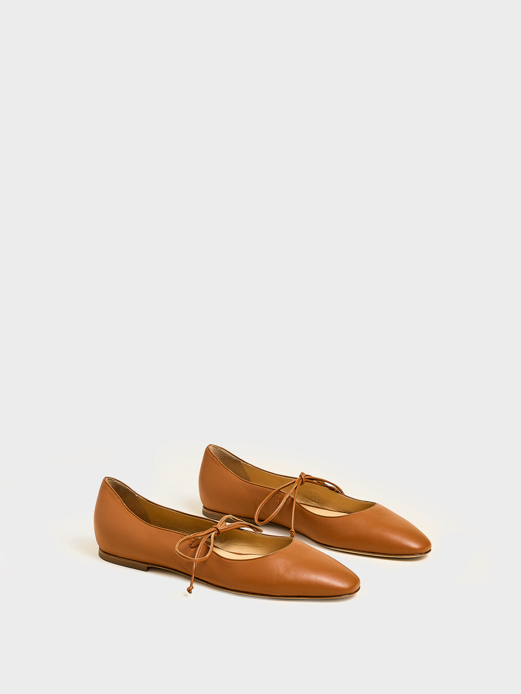 Angle view of a pair of chestnut suede ballet flats with an almond toe and tie detail.