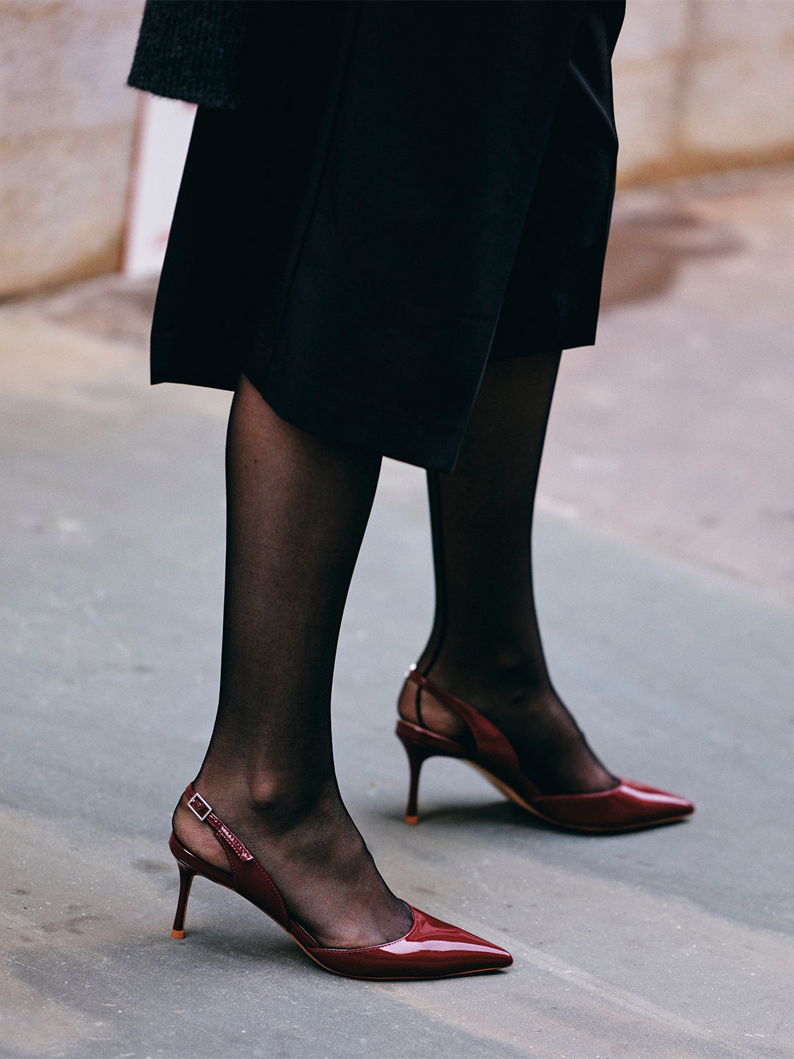 Side view of merlot red patent leather slingback heels with a pointed toe, shown on model.
