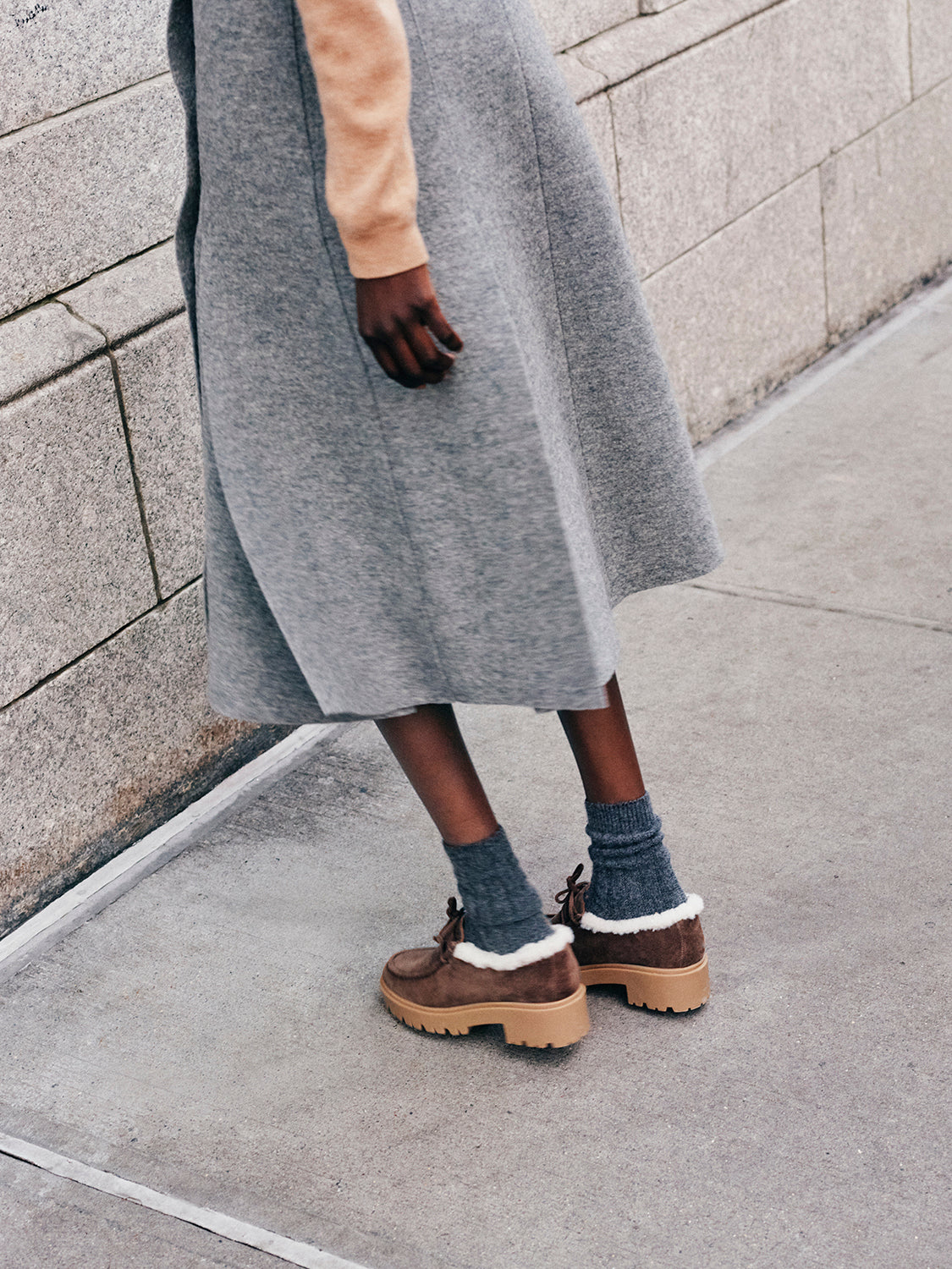 Woman wearing a wool skirt with brown suede shearling lined lug sole loafers.