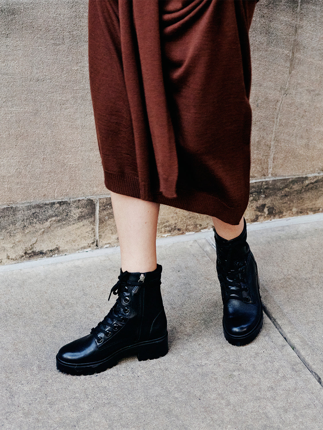Woman wearing a brown dress and black lug sole lace-up boots. 