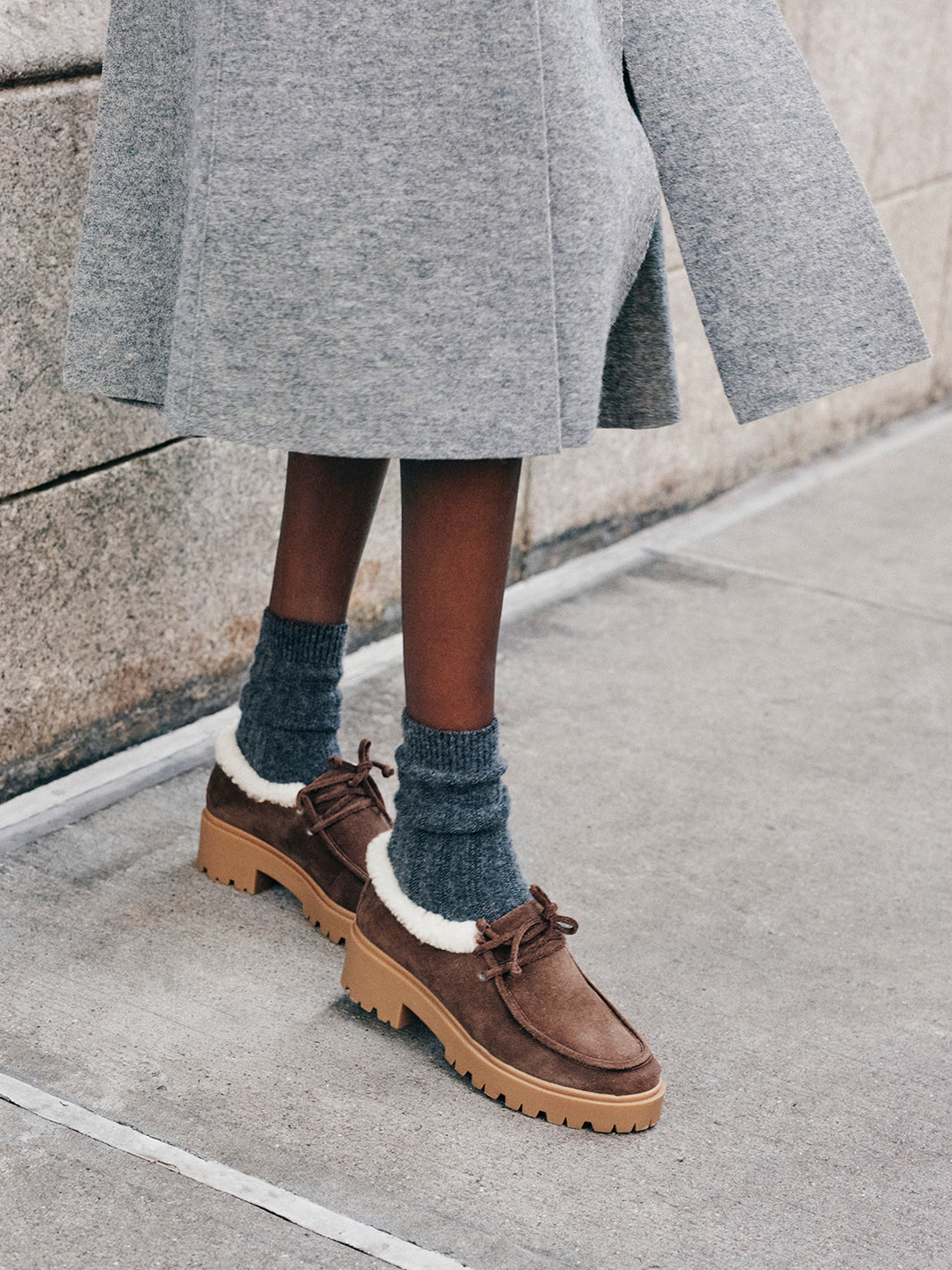 Woman wearing a wool skirt with brown suede shearling lined lug sole loafers.
