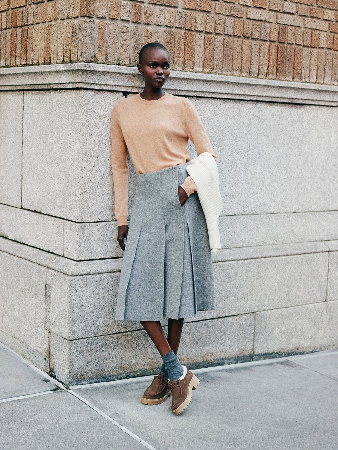 Woman wearing a beige sweater, wool skirt, and brown suede shearling lined lug sole loafers.