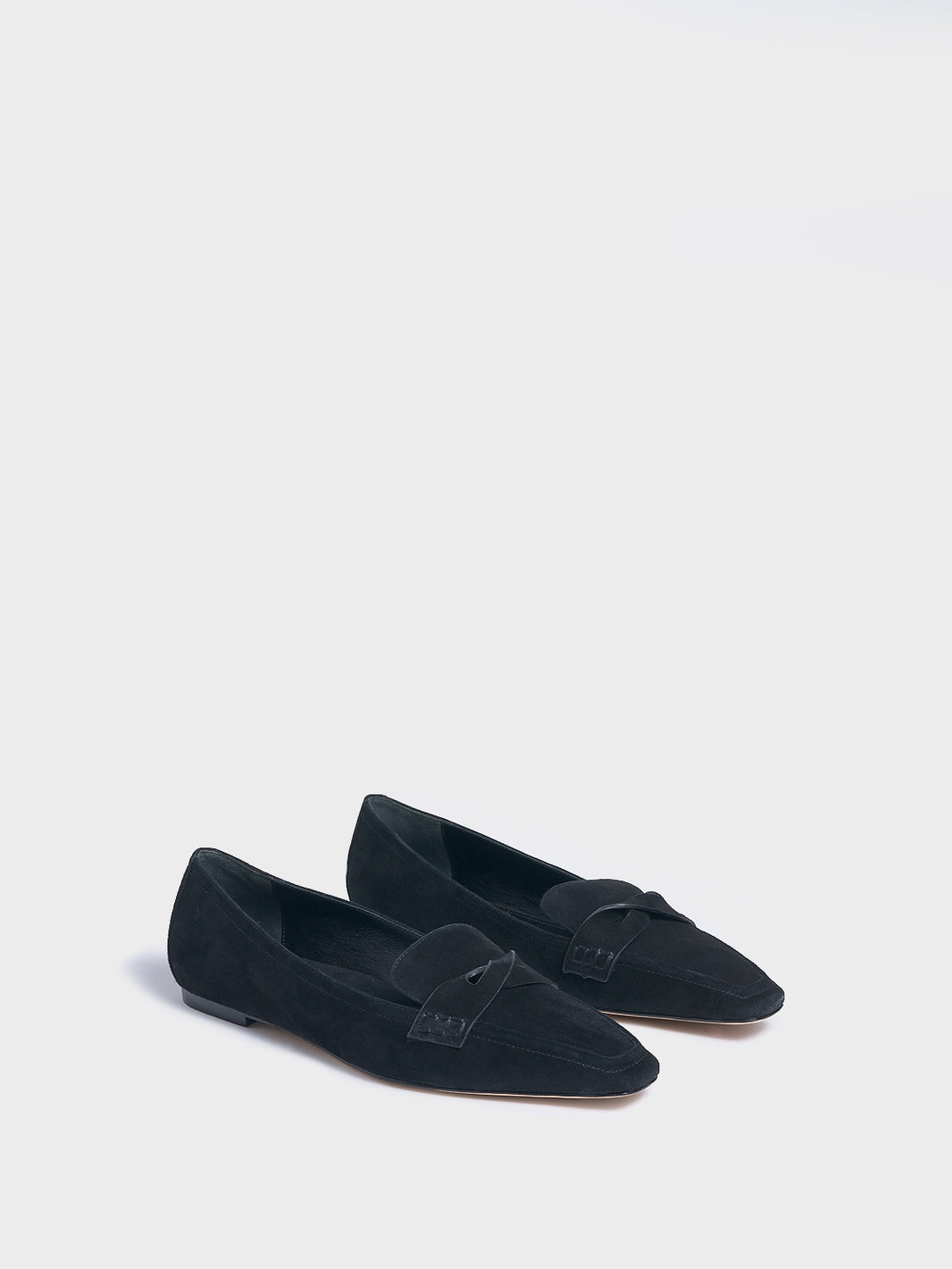 Angle view of a pair of black suede penny loafers with a twist detail.