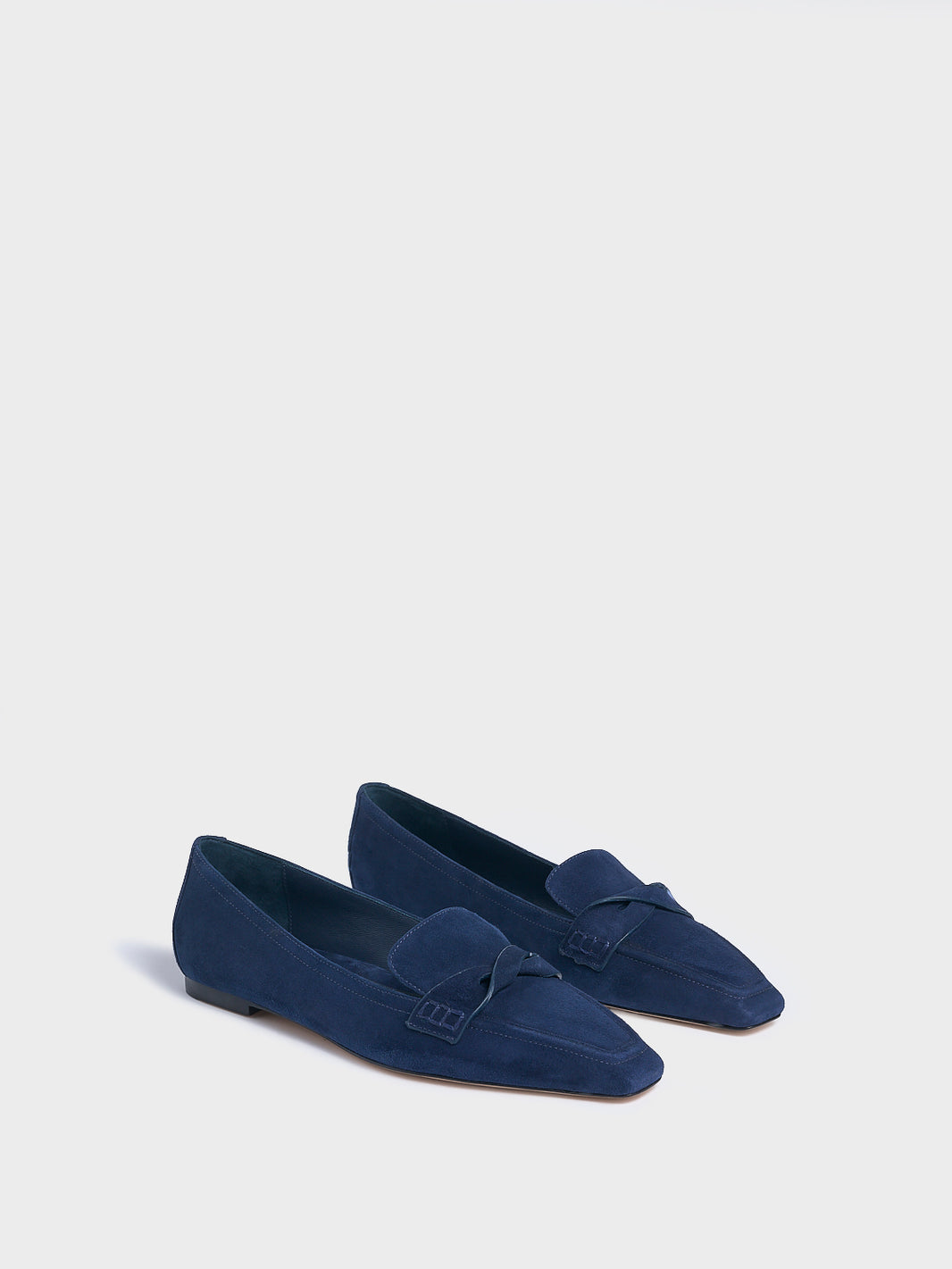 Angle view of a pair of navy blue suede penny loafers with a twist detail.