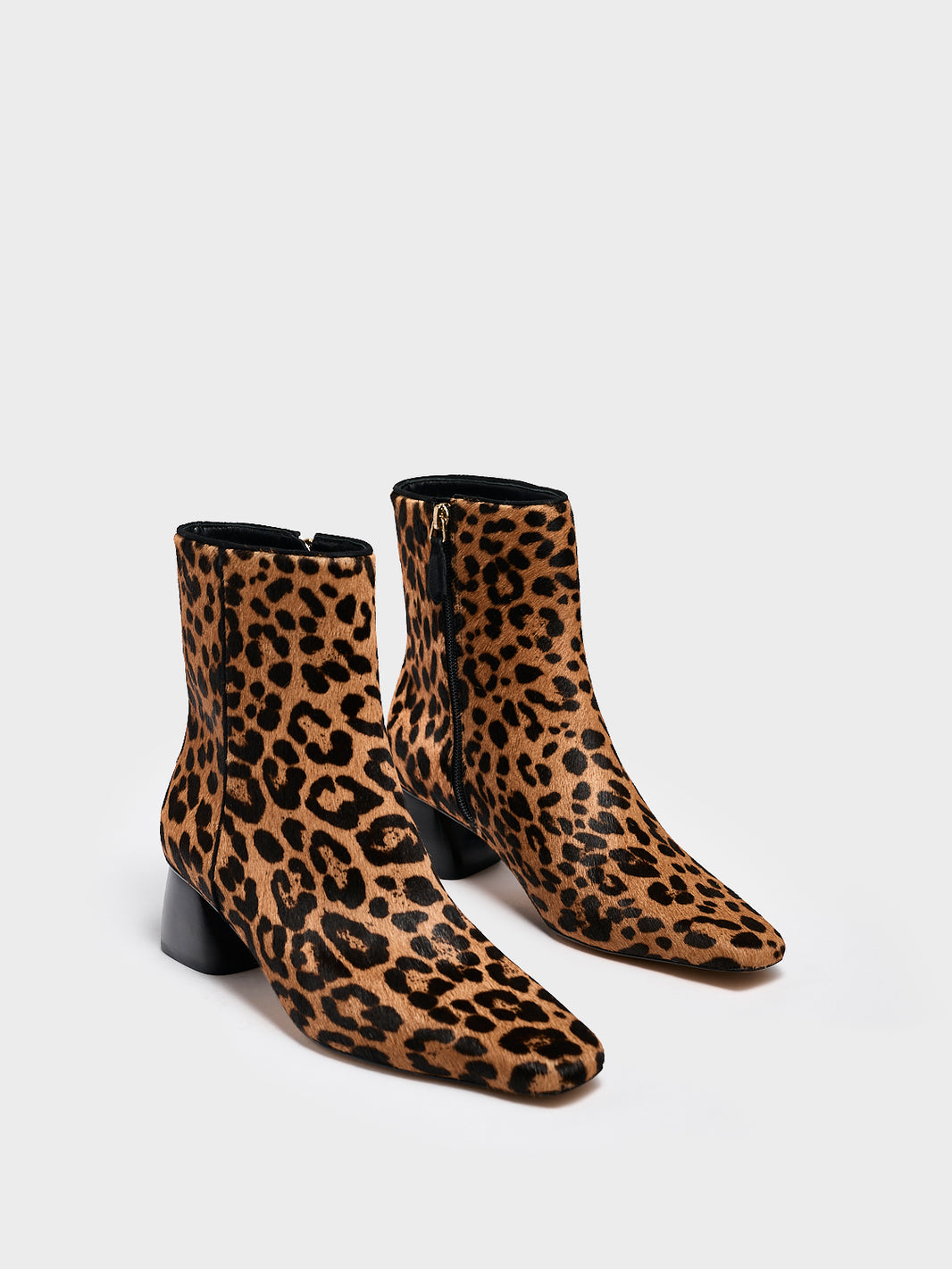 Angle view of a pair of leopard hair calf ankle booties with a rounded heel shape, zipper closure, and square toe. 