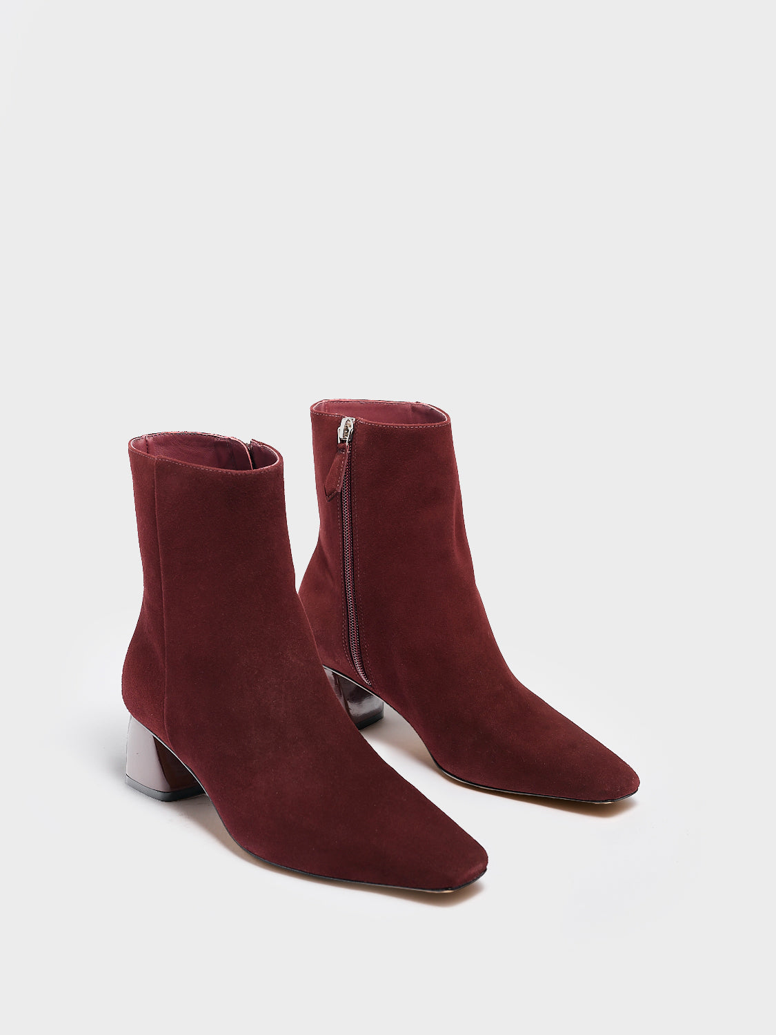 Angle view of a pair of merlot suede ankle booties with a rounded heel shape, zipper closure, and square toe. 