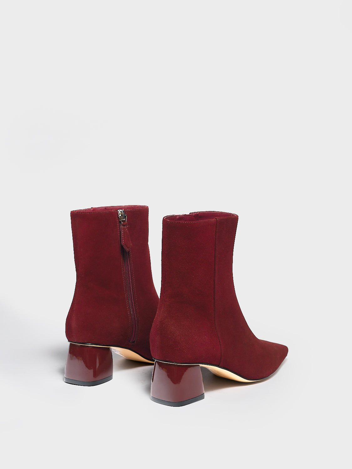 Back view of a pair of merlot suede ankle booties with a rounded heel shape, zipper closure, and square toe. 