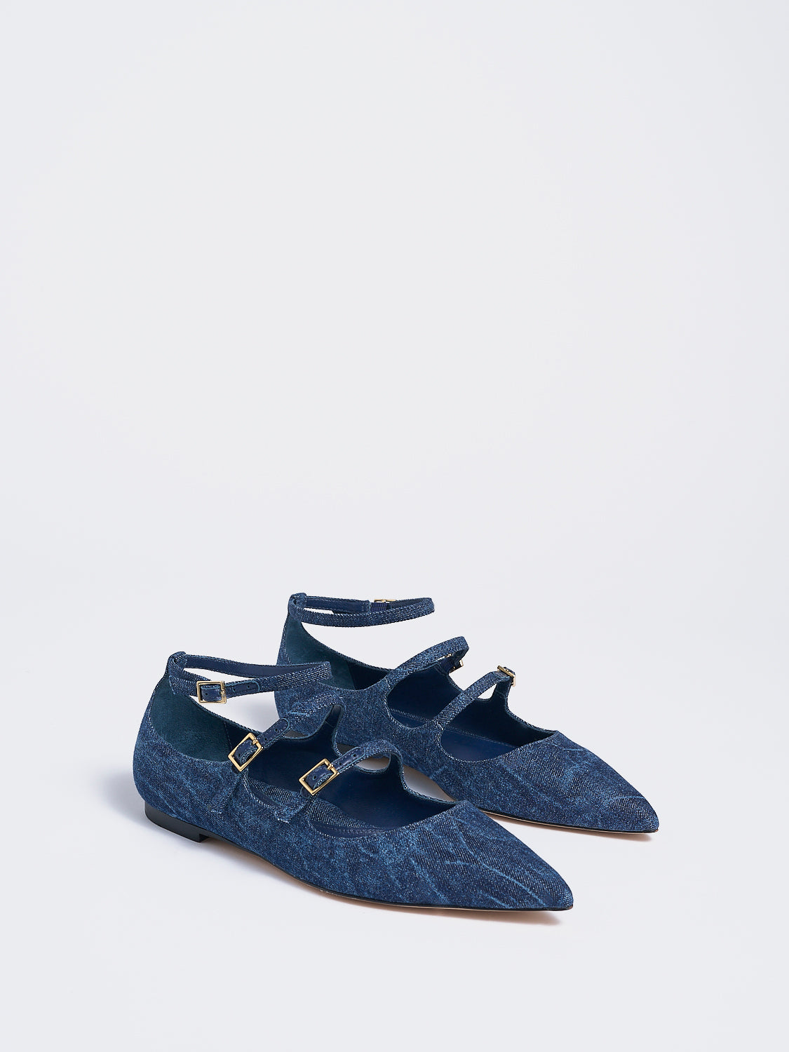 Angle view of a pair of navy denim mary jane flats with adjustable straps and a pointed toe. 