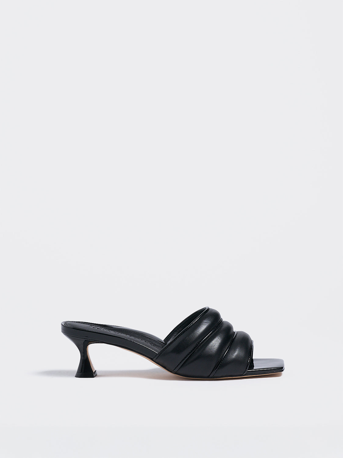 Profile view of a black leather slide kitten heel with a patent leather trimmed puffy strap detail.