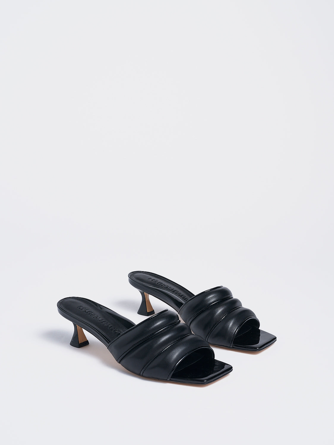 Angle view of a pair of black leather slide kitten heels with a patent leather trimmed puffy strap detail.