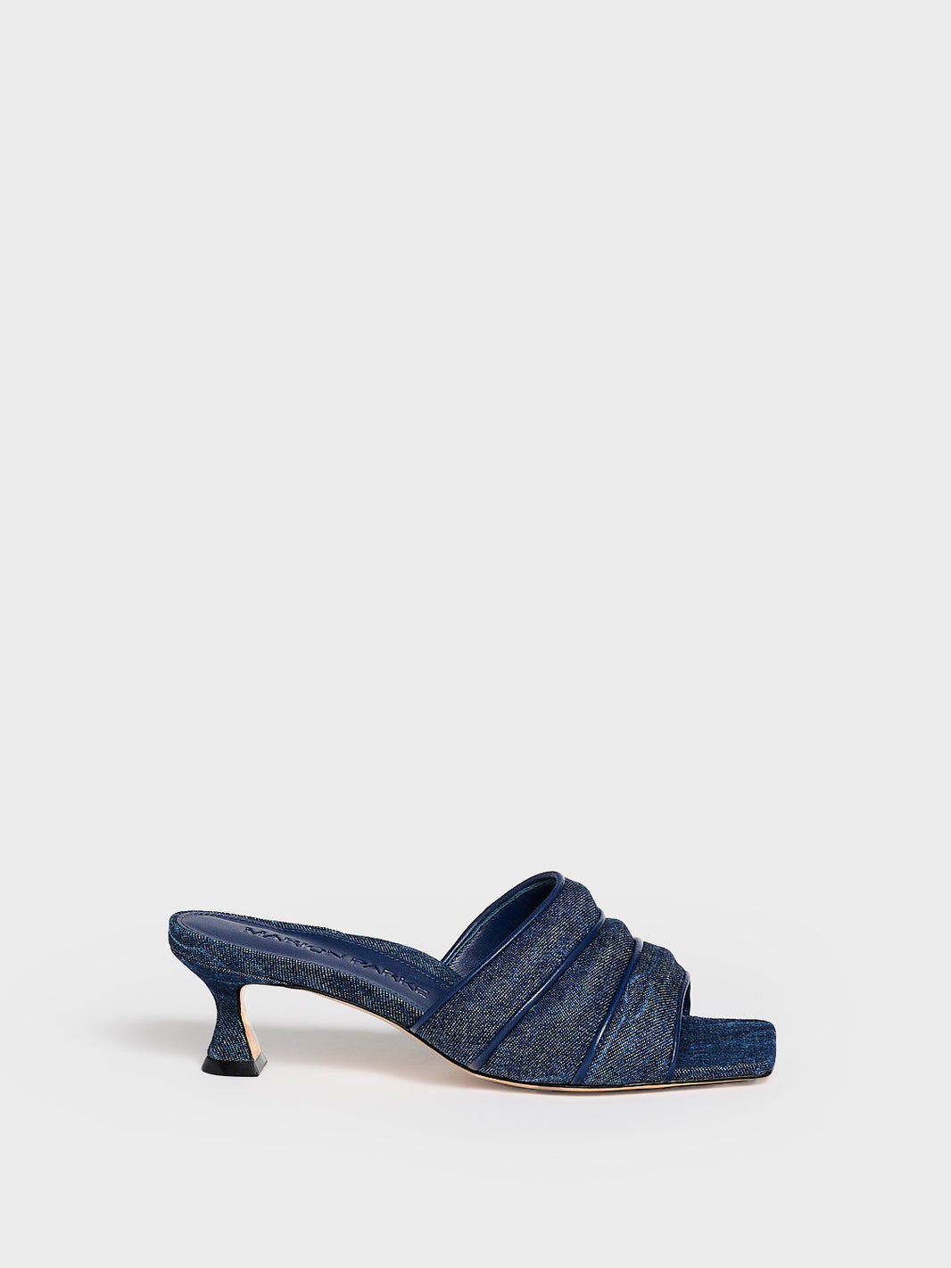 Profile view of a blue denim slide kitten heel with a leather trimed puffy strap detail.