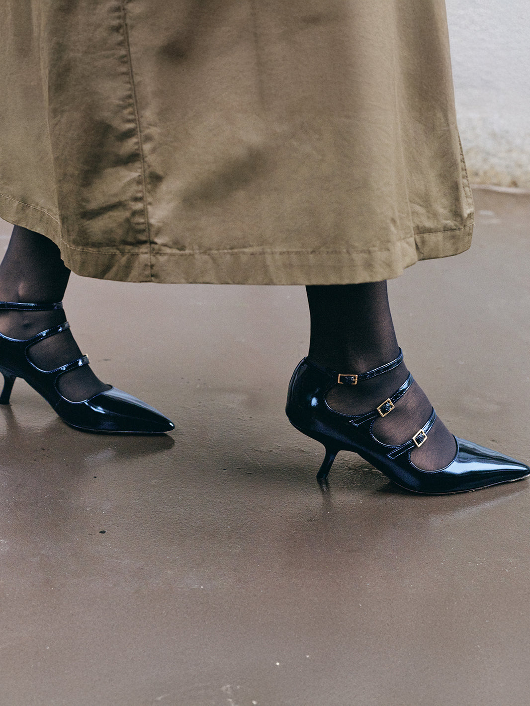 Side view of a black leather  mary jane heels with adjustable straps and a pointed toe, shown on a model.