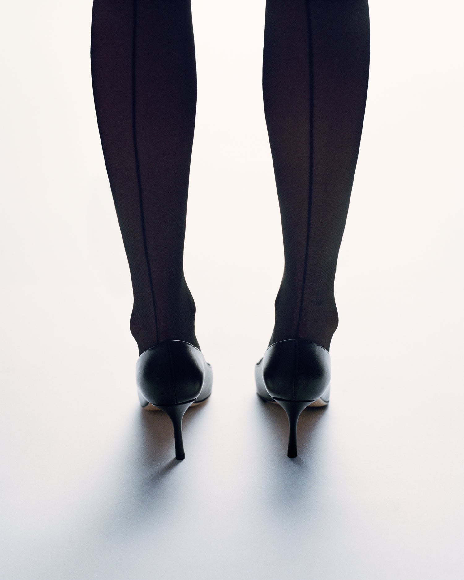 Woman wearing a black leather stiletto heel pump with a gold metallic toe cap and a pointed toe.