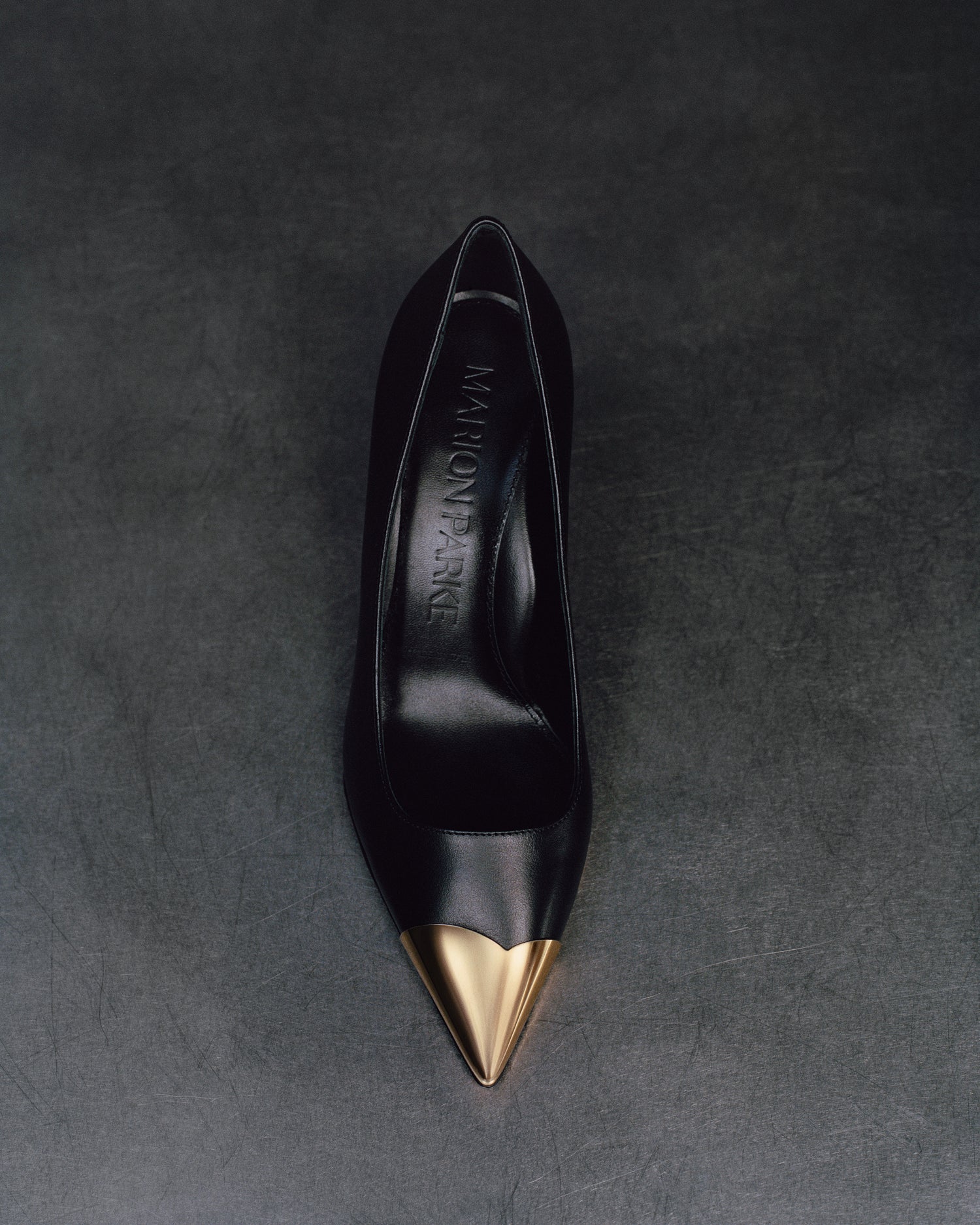 Top view of a black leather stiletto heel pump with a gold metallic toe cap and a pointed toe.