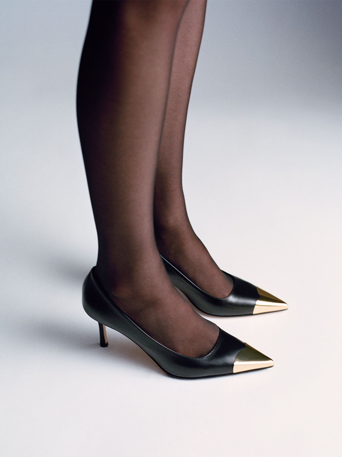 Black leather pumps with a gold metal toe cap, shown on a model.