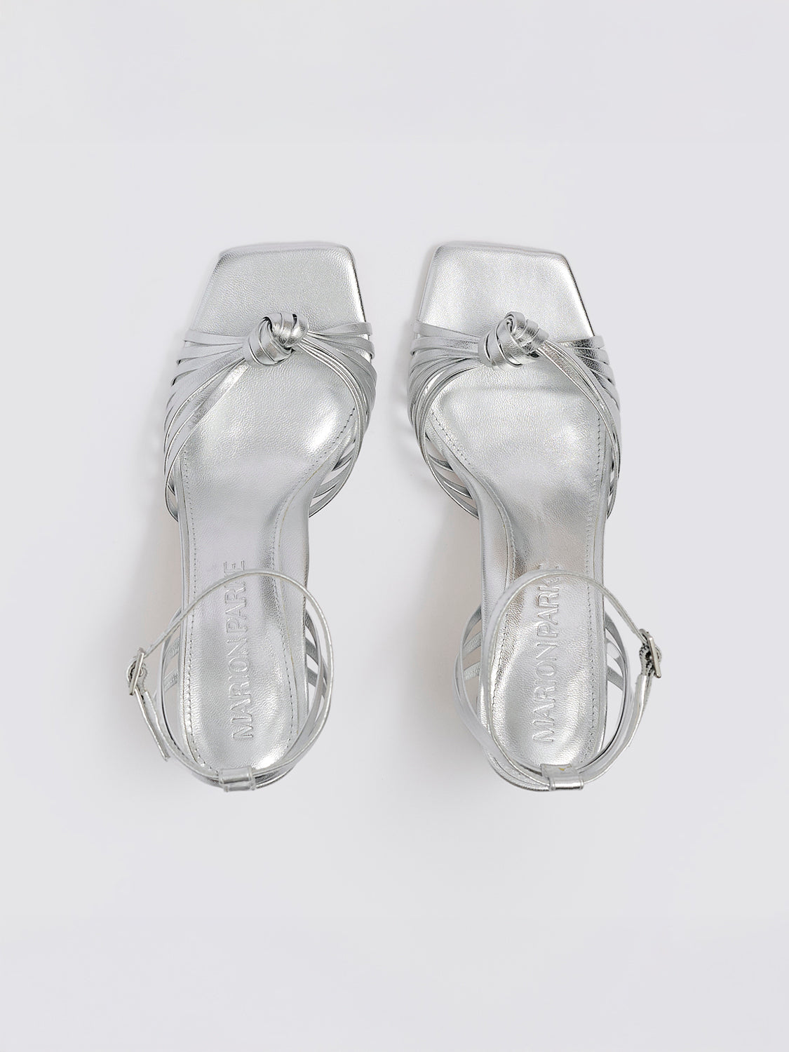 Top view of a pair of silver metallic leather block heel sandals with a knot detail and a square toe