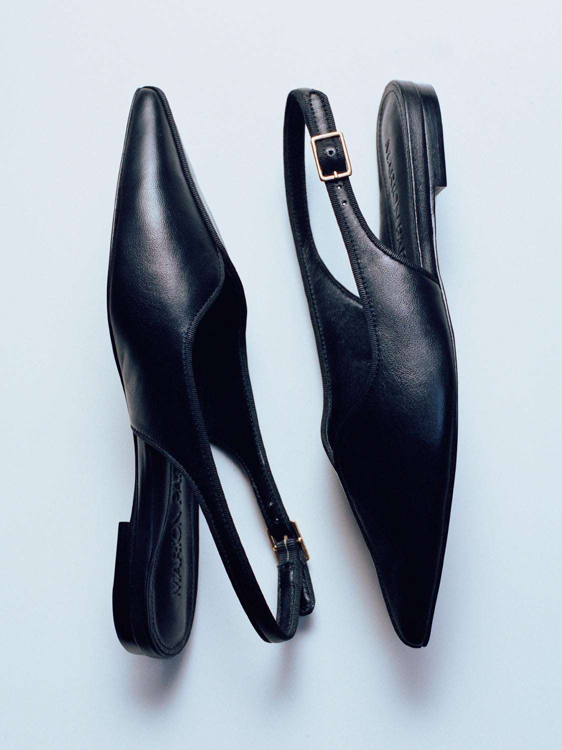 Side view of a pair of black leather slingback flats with a grosgrain trim detail.