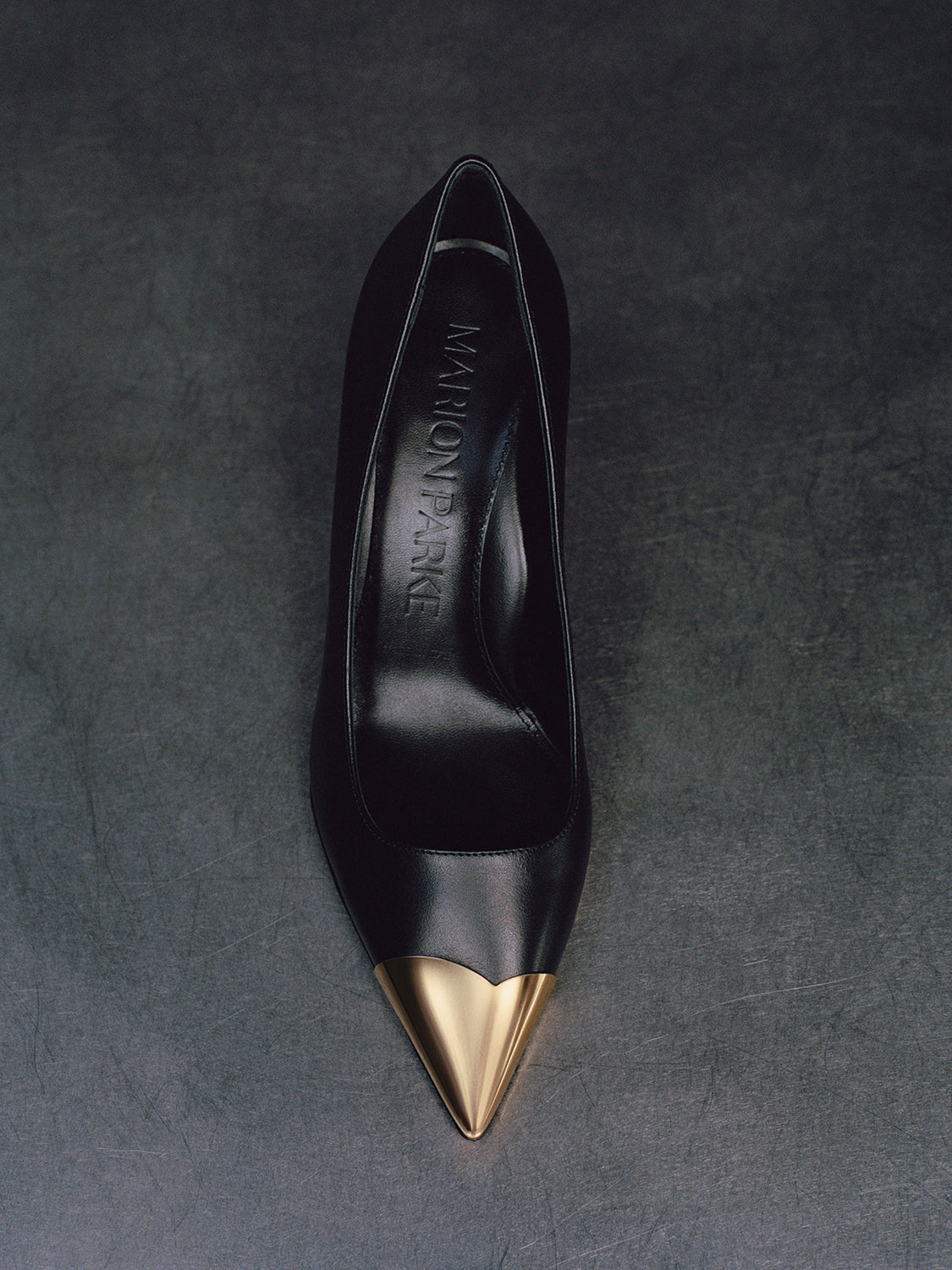 Top view of a black leather pump with a gold metal toe cap. 