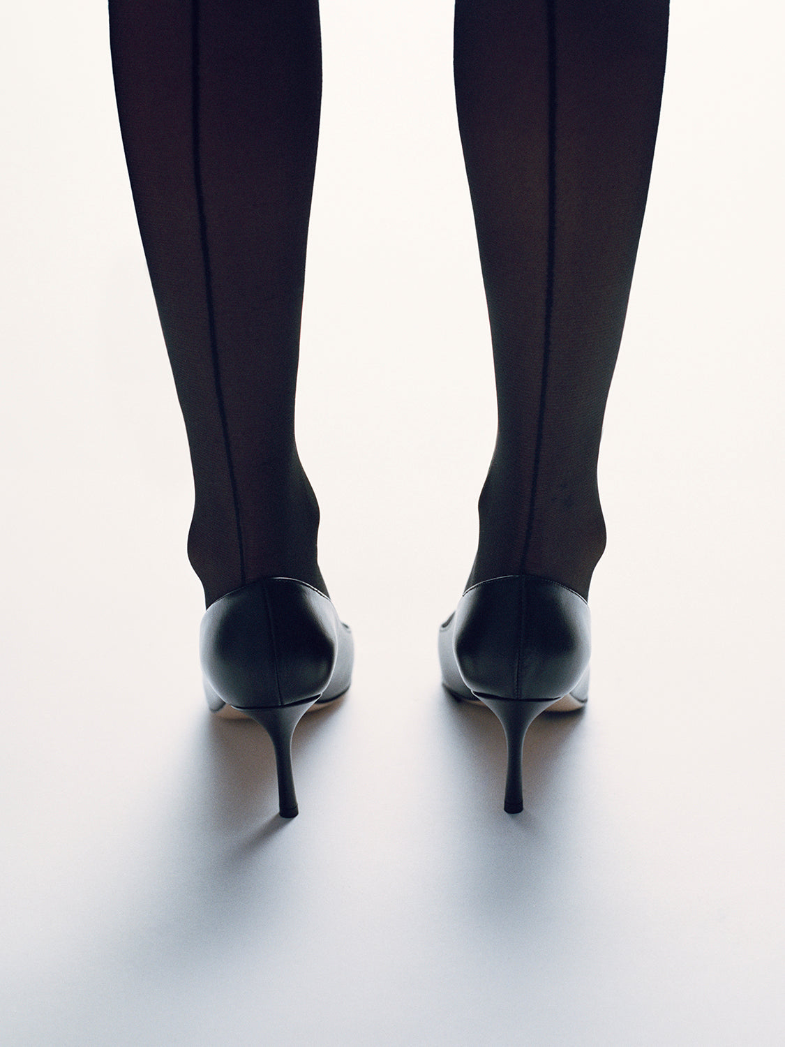 Back view of a black leather pumps with a gold metal toe cap. 