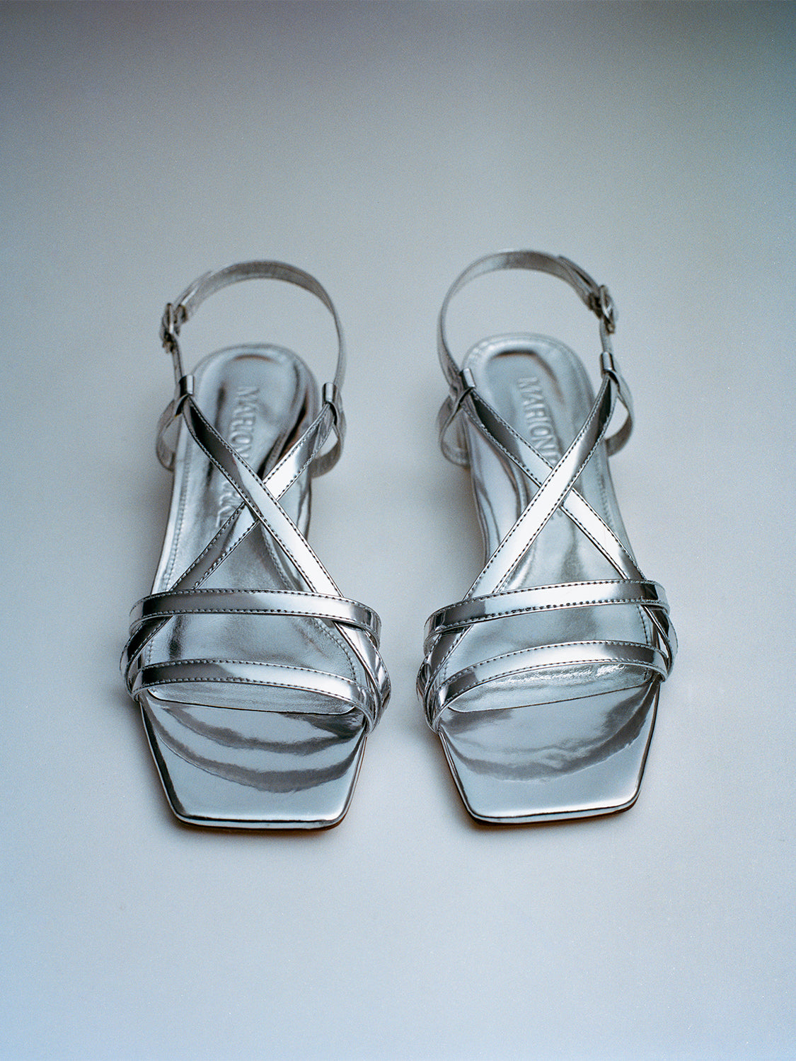 Top view of a pair of silver metallic leather flat strappy sandals.