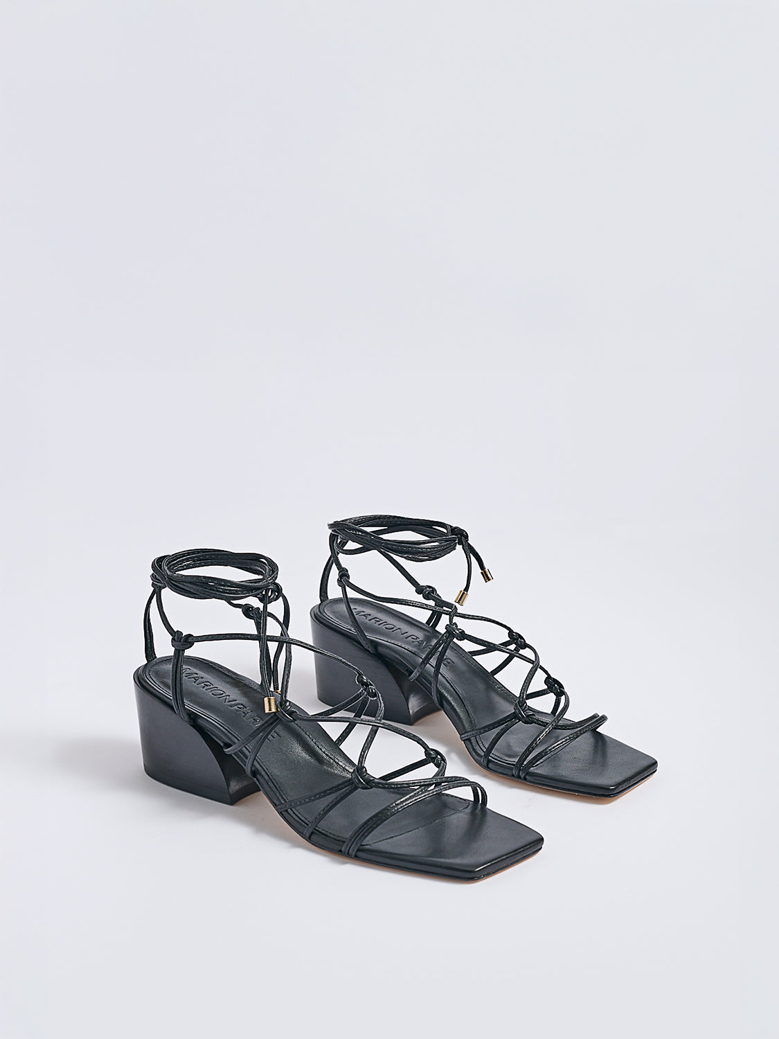 Angle view of a pair of black leather lace up block heel sandals with a square toe