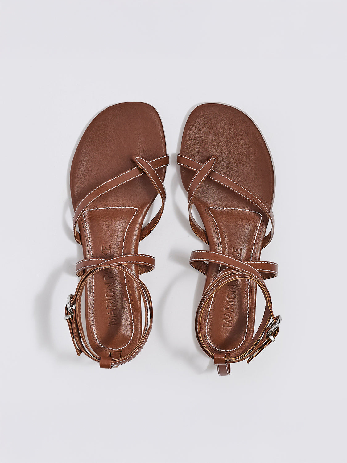 Top view of a pair of luggage leather thong flat sandals with a rounded toe