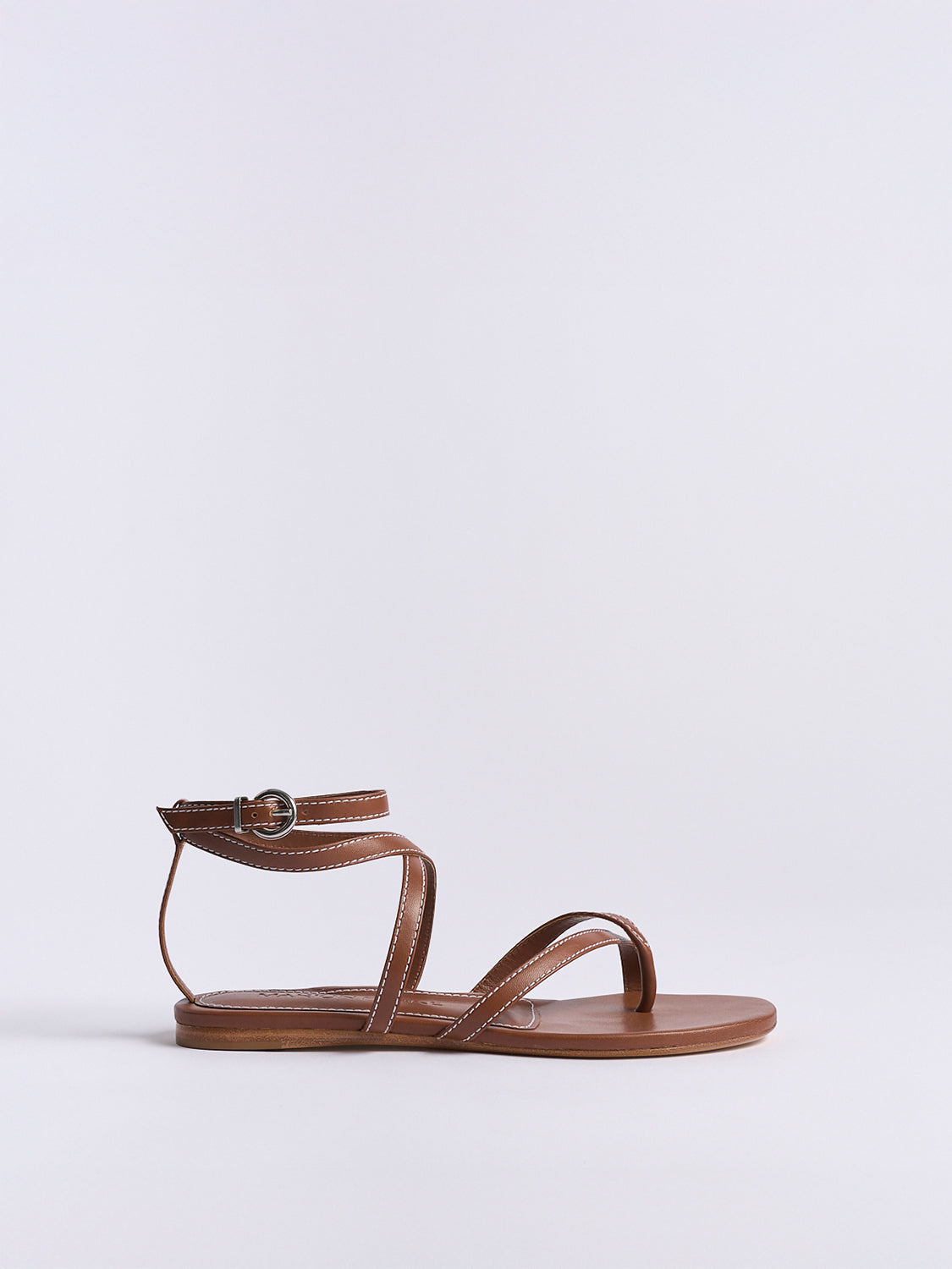 Profile view of a luggage leather thong flat sandal with a rounded toe