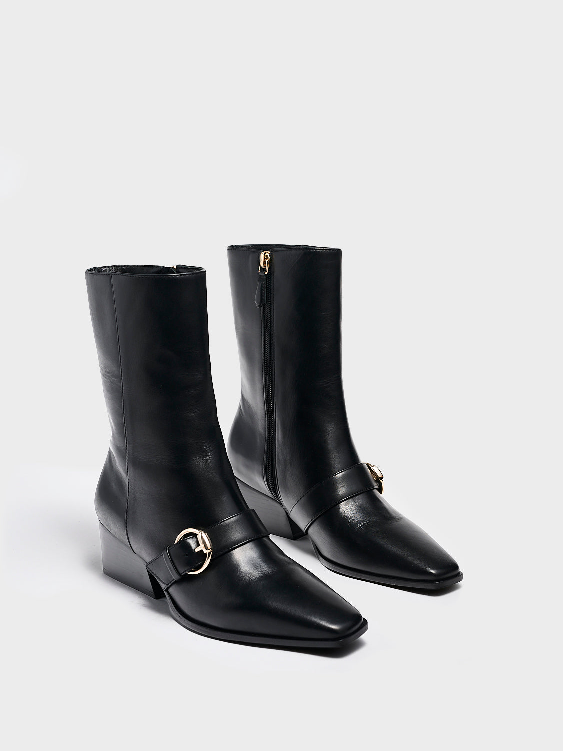 Angle view of a pair black nappa leather  ankle booties with a zipper closure, silver buckle, and block heel. 