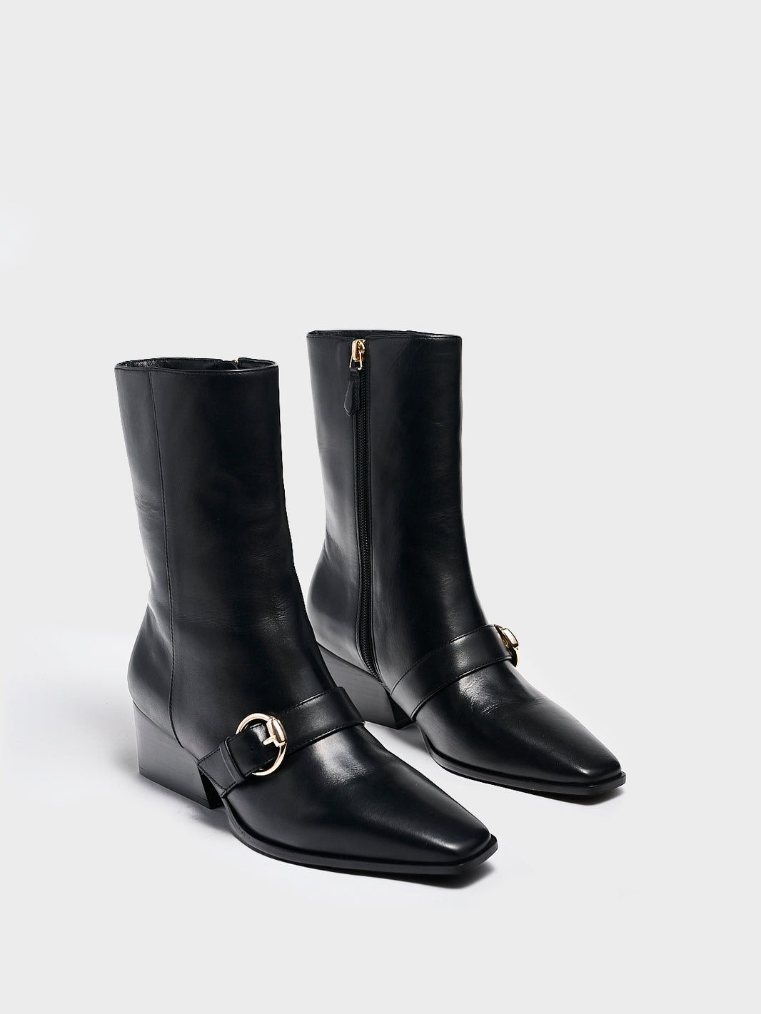 Angle view of a pair black nappa leather  ankle booties with a zipper closure, silver buckle, and block heel. 