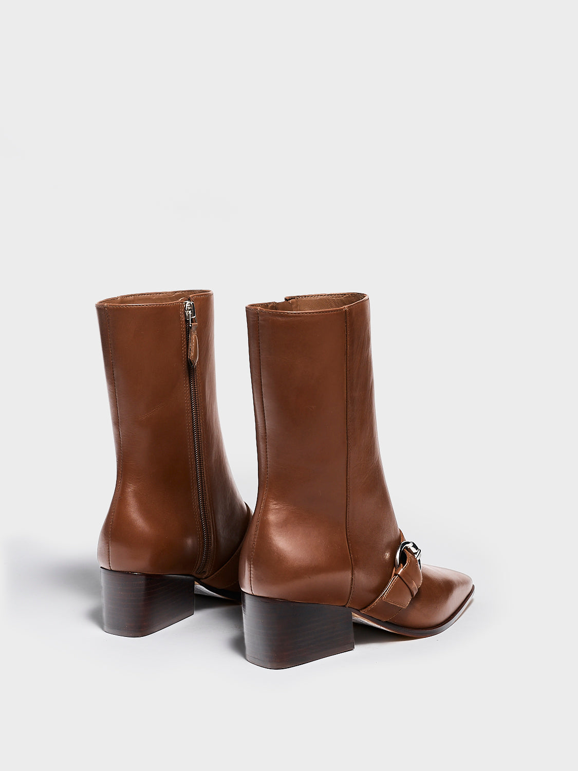 Back view of a mocha brown nappa leather ankle bootie with a zipper closure, silver buckle, and block heel. 